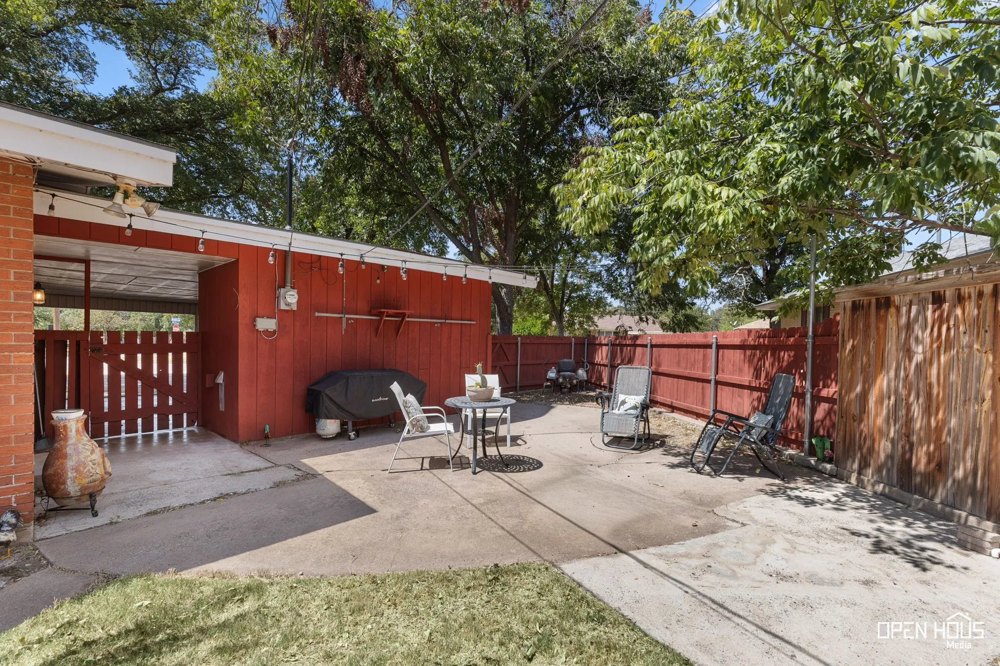 Paved patio area with a covered section, wood fencing, and mature trees