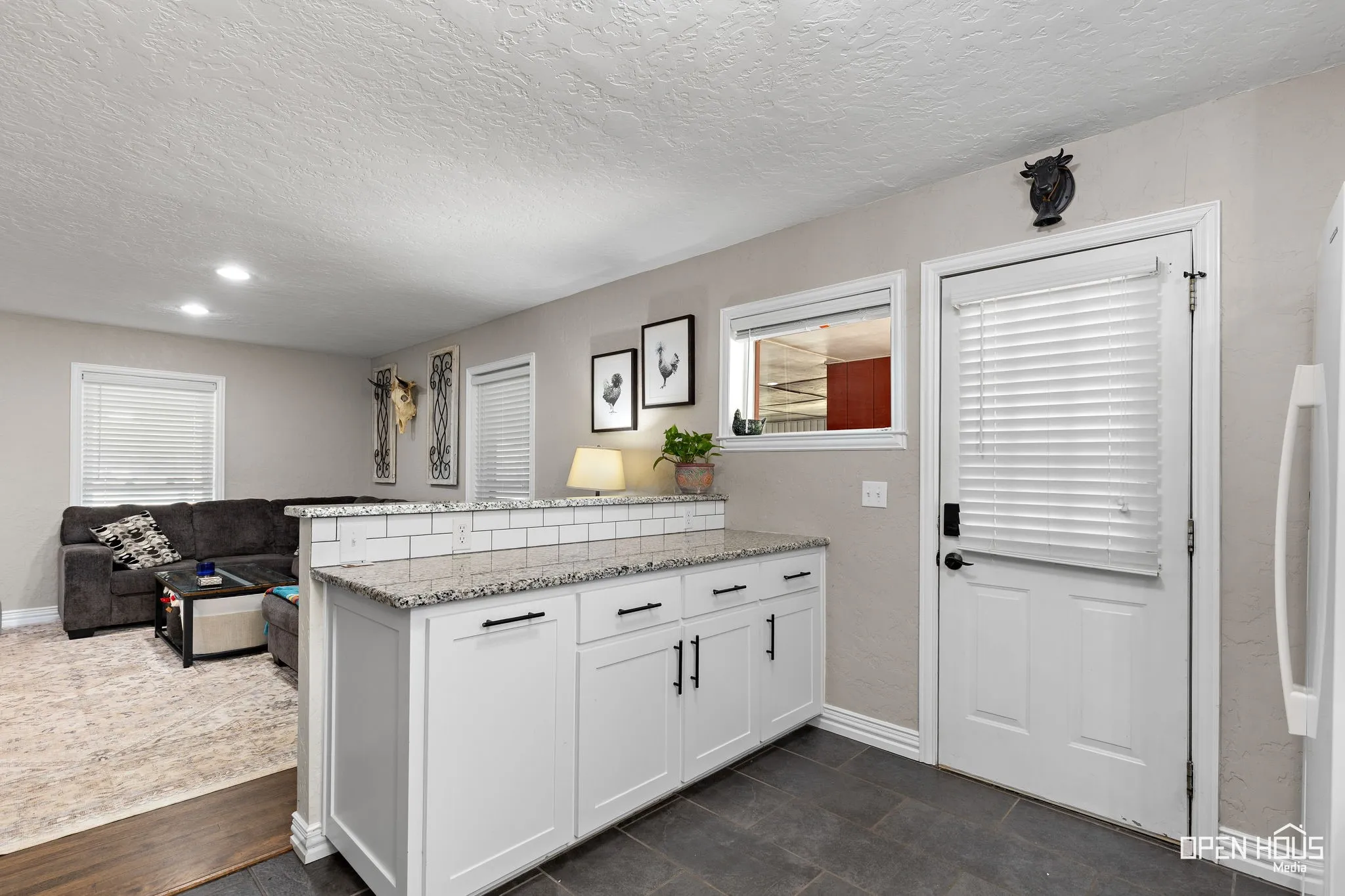 White shaker-style cabinetry with black hardware, granite-style countertop, white subway tile backsplash, recessed lighting, and tile flooring