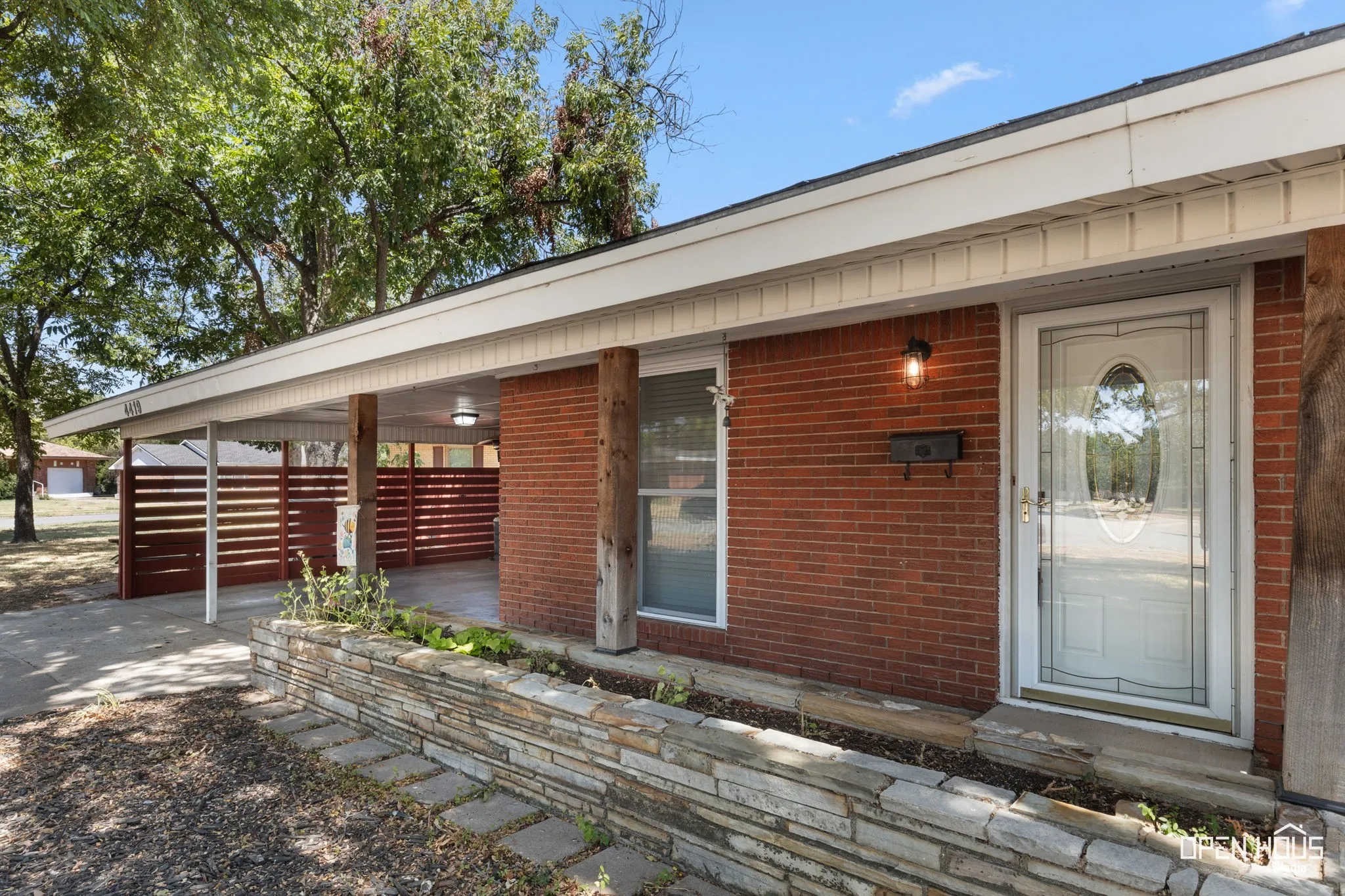 Brick exterior with a covered carport, decorative wood screen, and stone planter