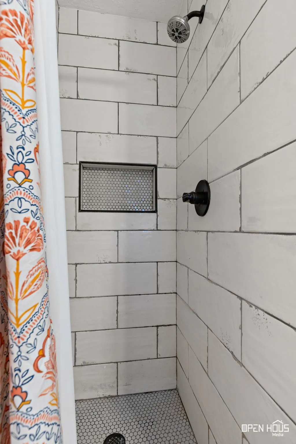 White subway tile shower walls with a built-in niche, black fixture, and penny tile flooring