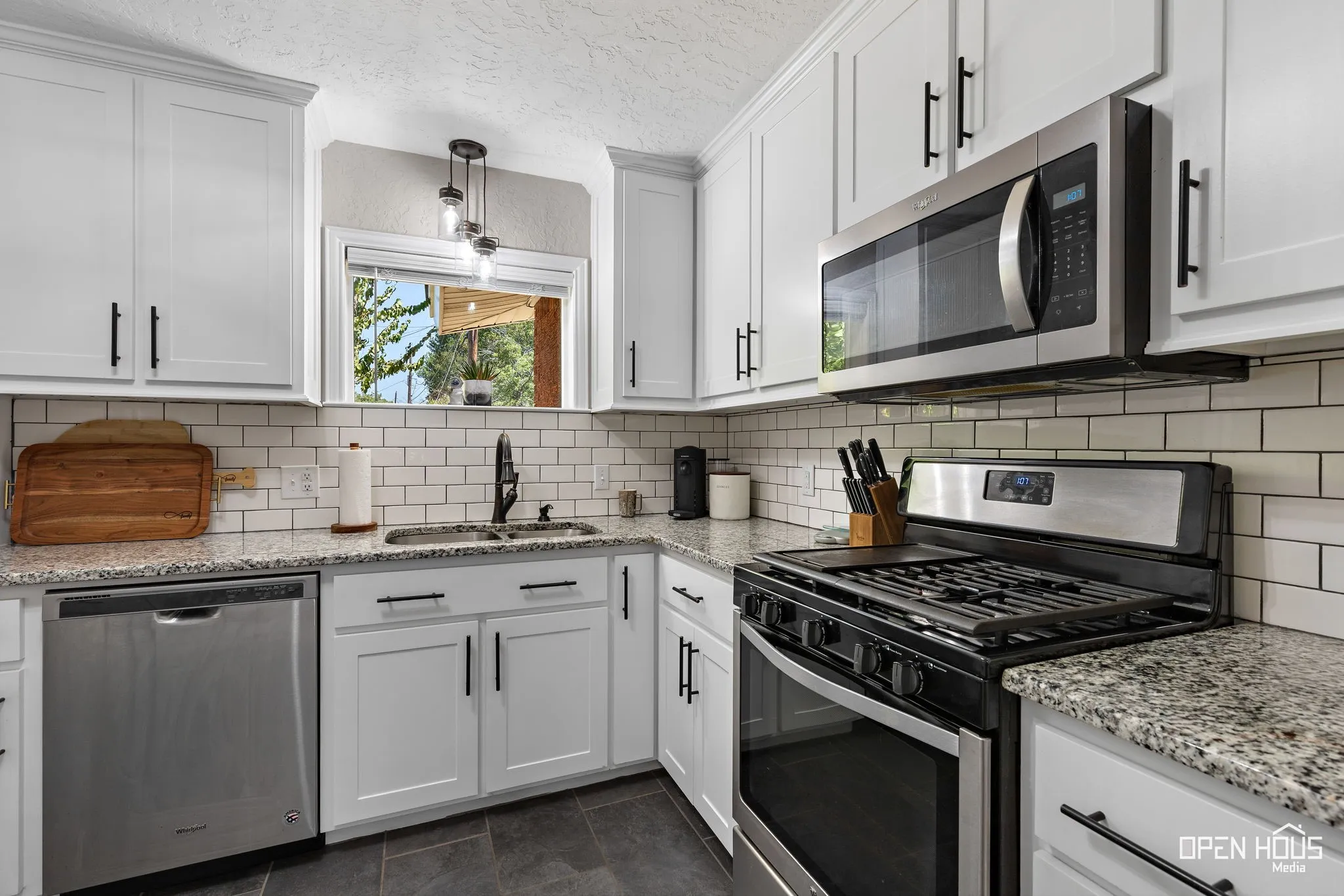 White shaker-style cabinetry with matte black hardware, stainless steel appliances, granite countertops, and a subway tile backsplash
