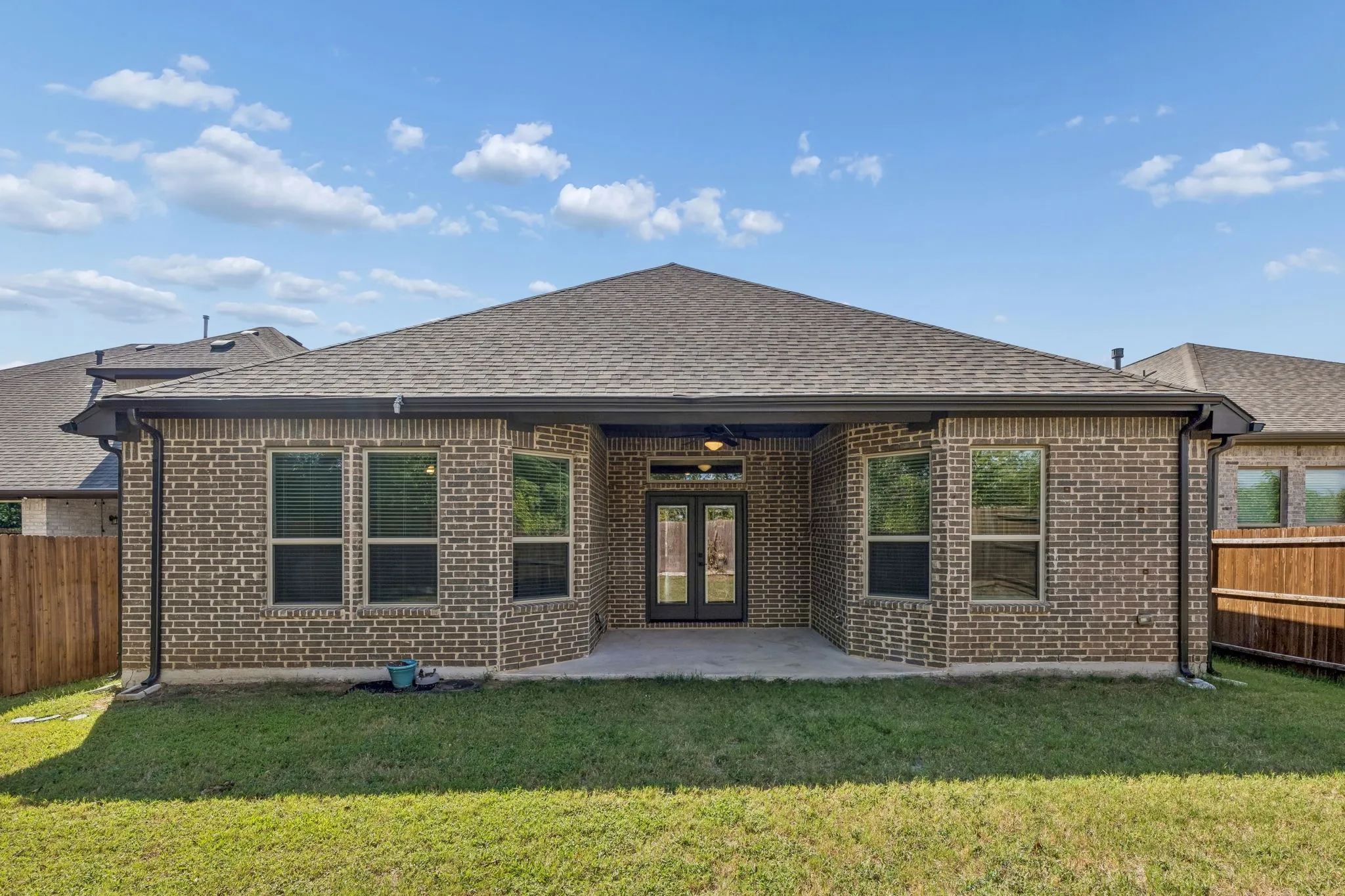 Brick exterior with a covered patio, multiple windows, and a shingled roof