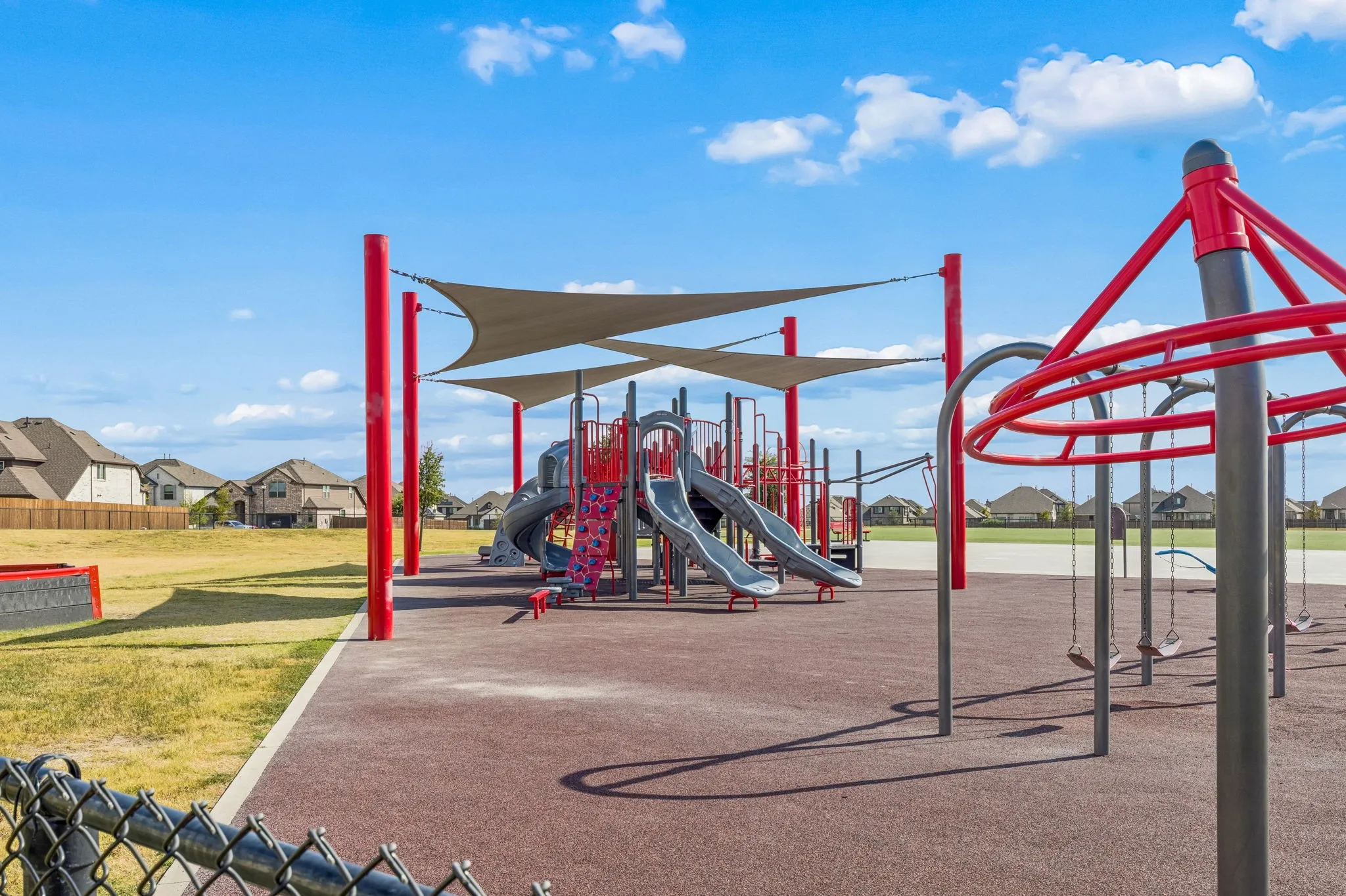 Community playground featuring a multi-level play structure, slides, swings, and shade sails