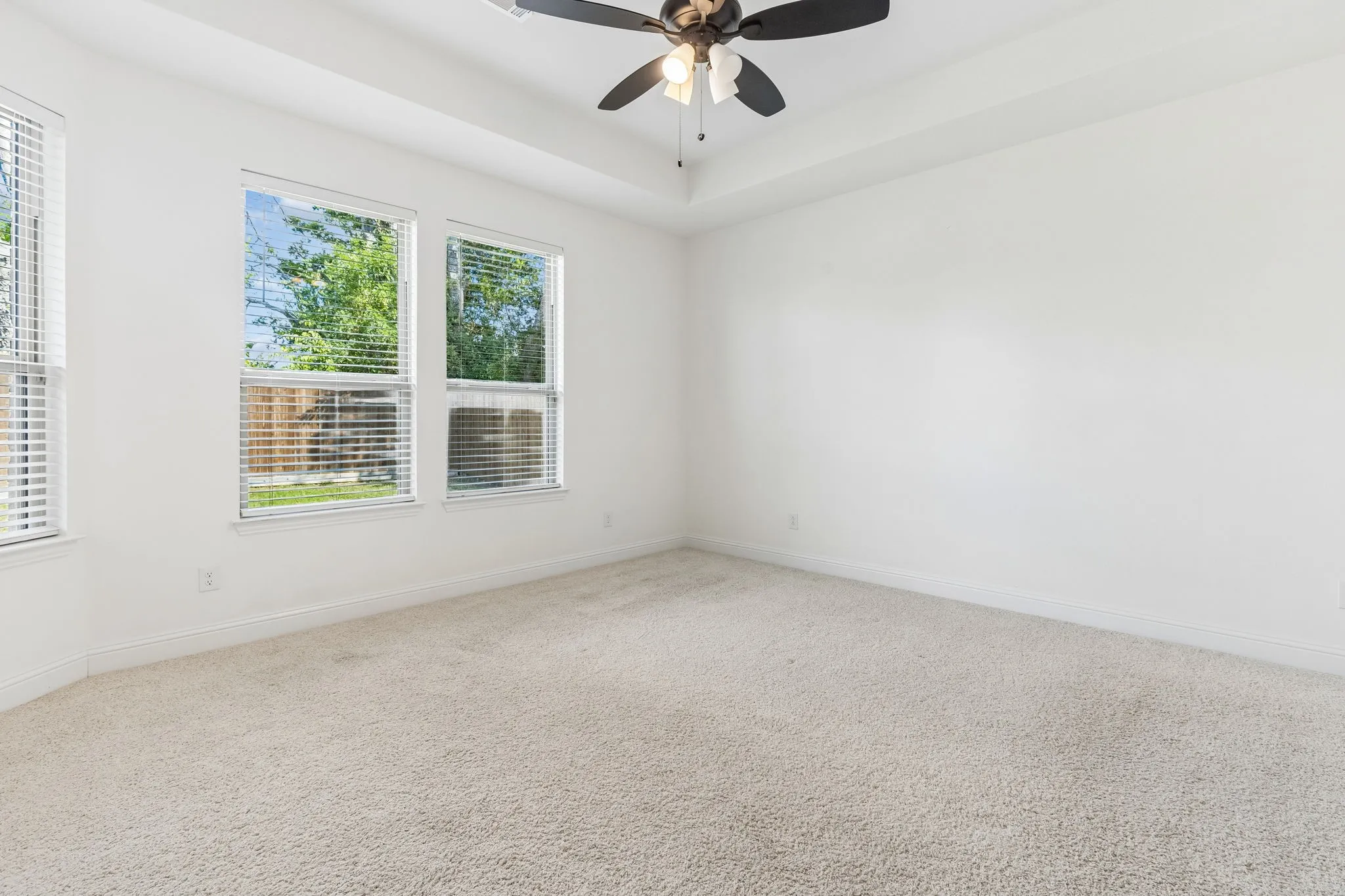 Recessed ceiling, neutral carpeting, multiple windows with blinds, ceiling fan with light fixture