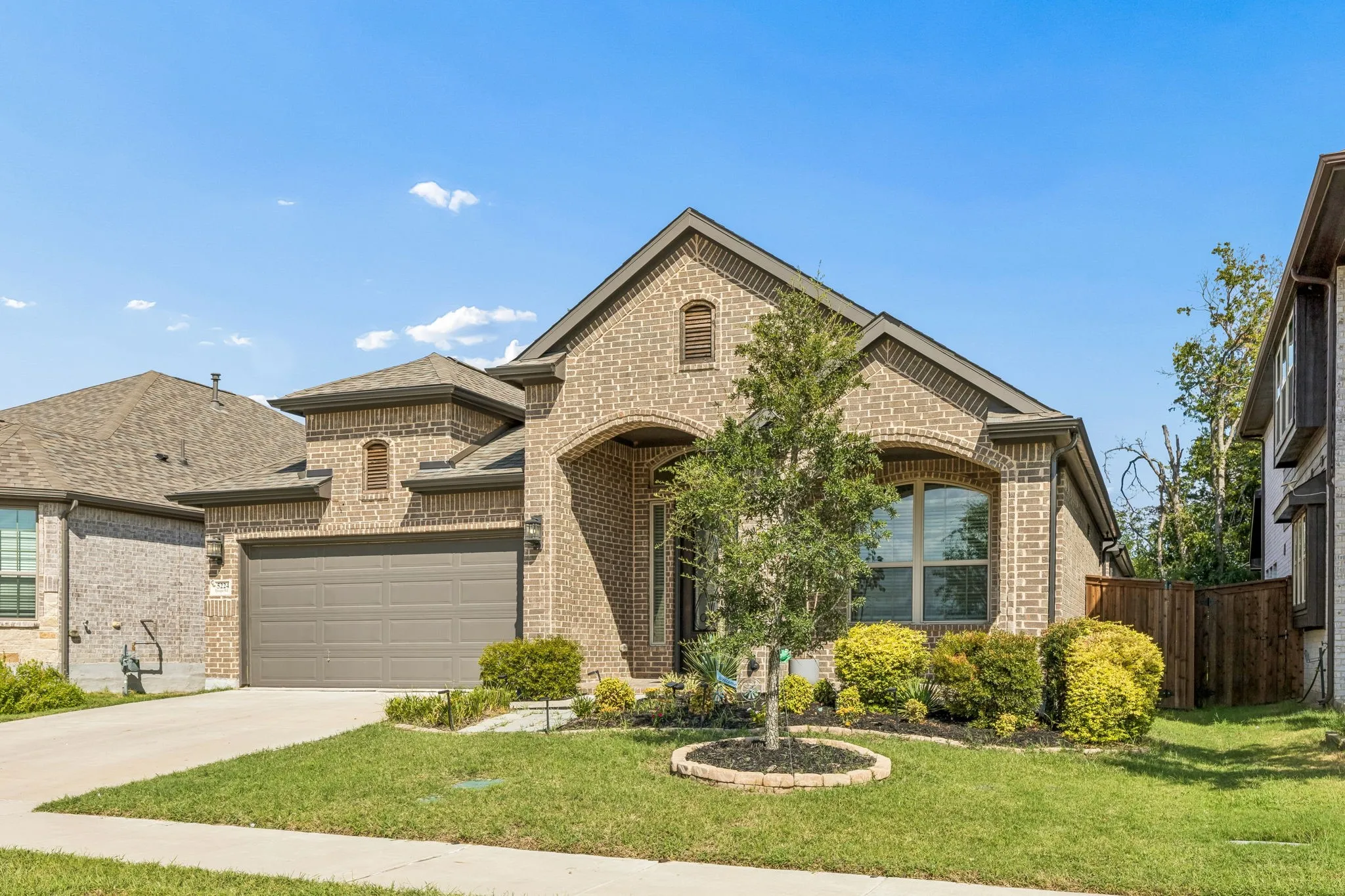 Brick exterior with stone accents, arched entry, two-car garage, and established landscaping