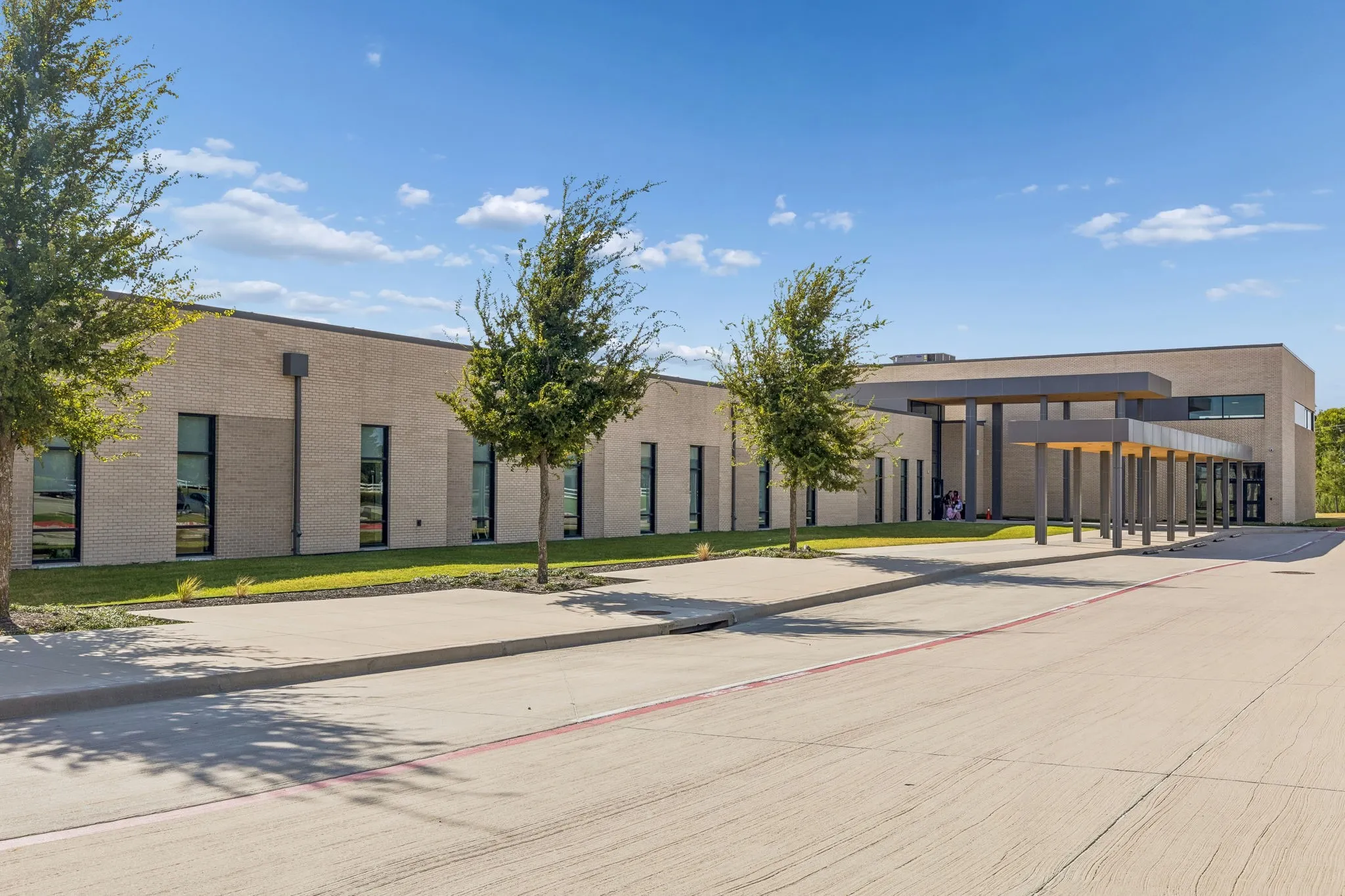 Modern brick exterior with expansive windows, an extended porte-cochere, and mature landscaping