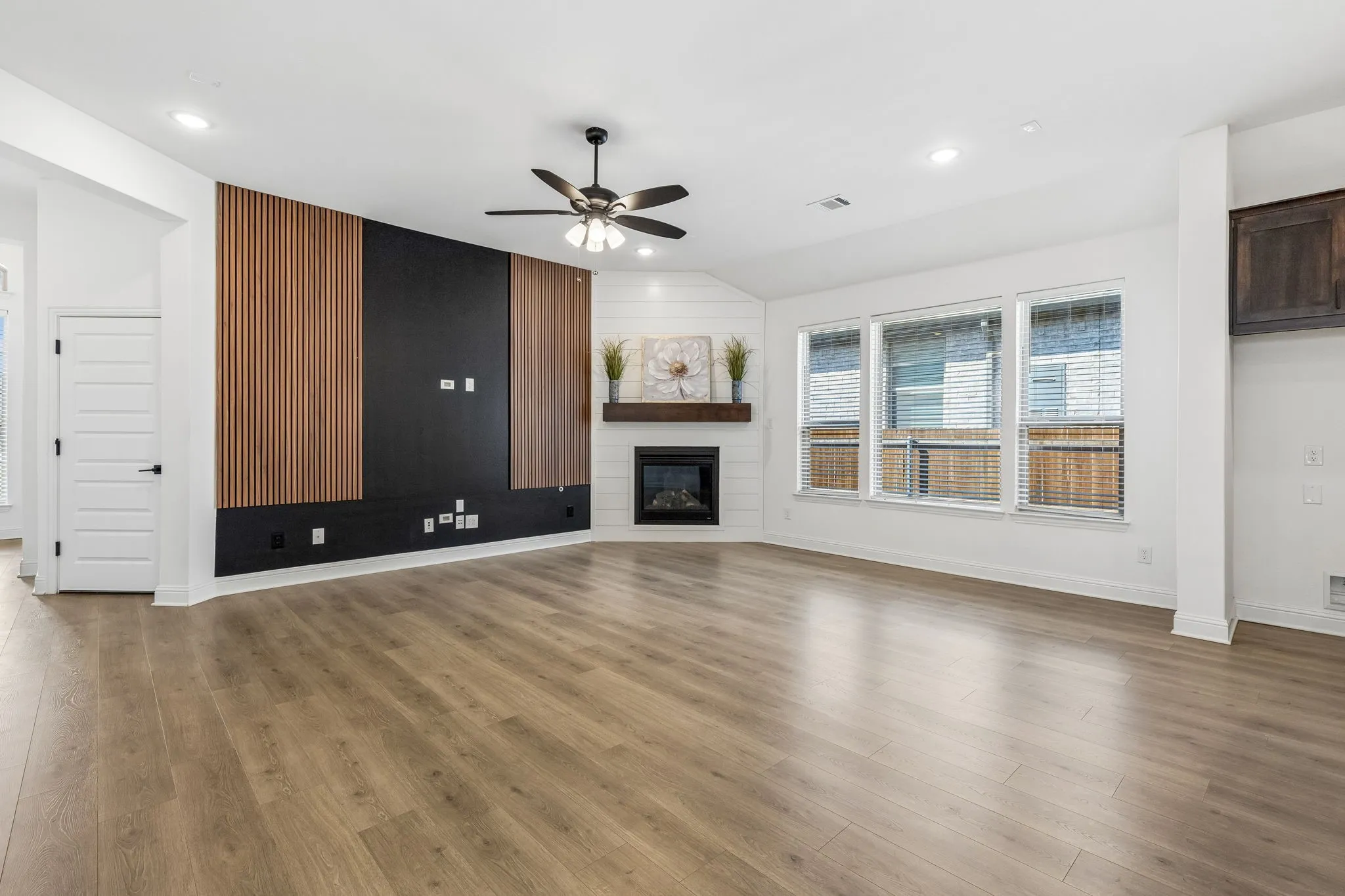 Wood-finish flooring throughout, modern media wall with wood slat accents, corner fireplace with a wood mantle, white shiplap wall detail, and recessed lighting