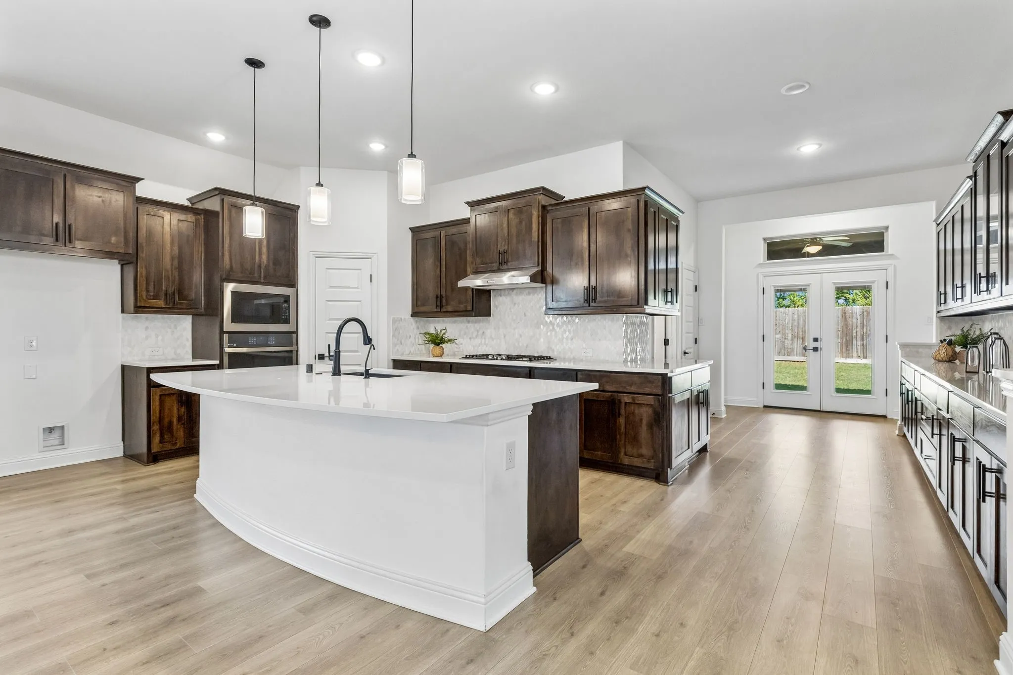 Modern kitchen featuring a large central island with a solid surface countertop, dark wood-finish cabinetry, and light wood-finish flooring