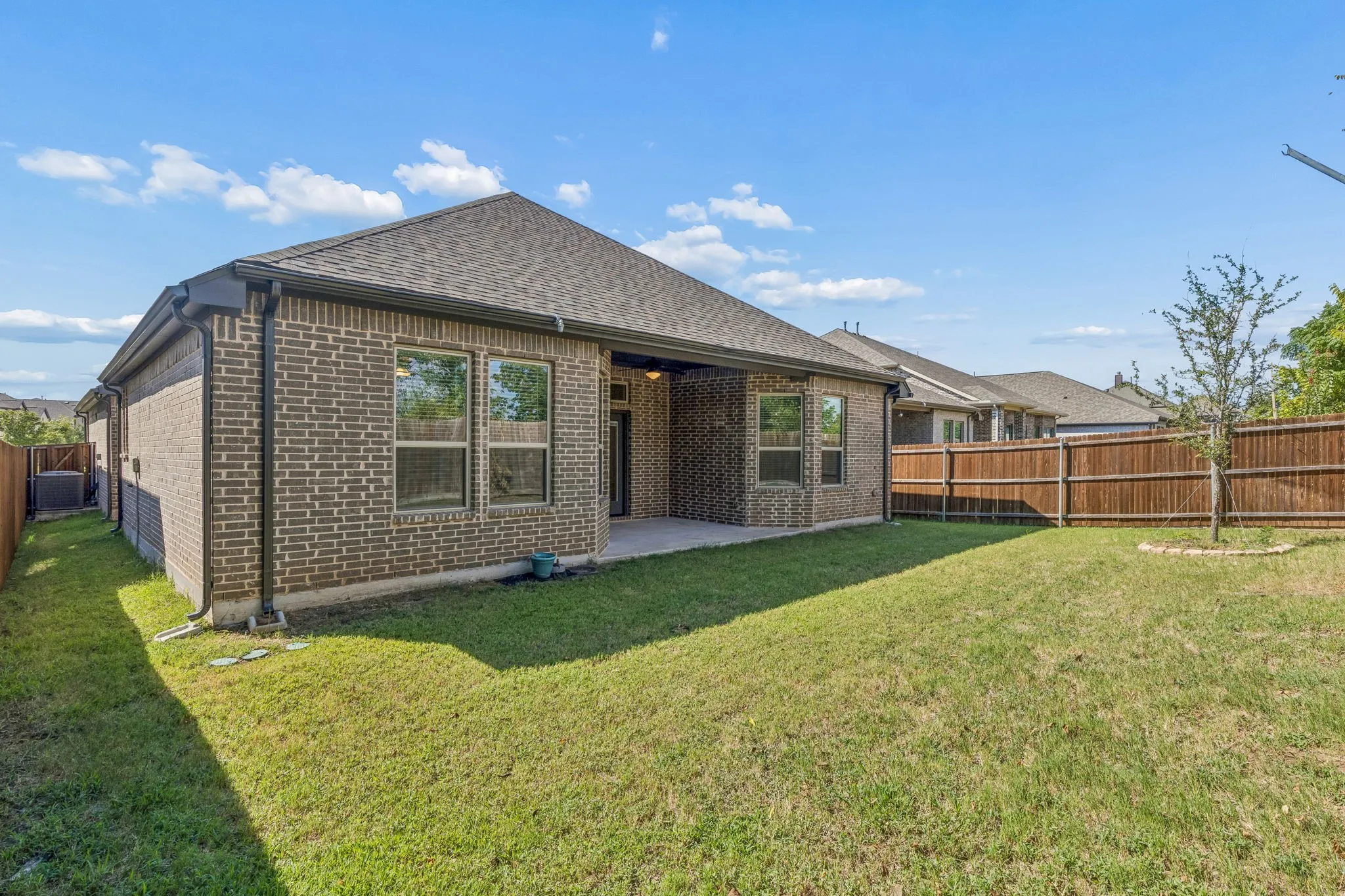 Brick exterior home featuring a covered patio, fenced yard, and a young tree
