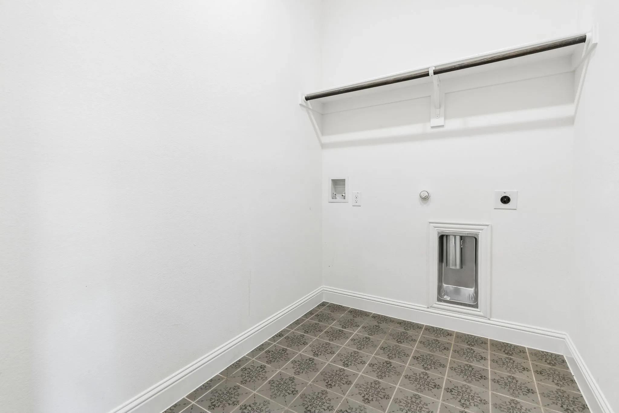 Laundry area with patterned floor tile, white walls, and a built-in shelf with hanging rod