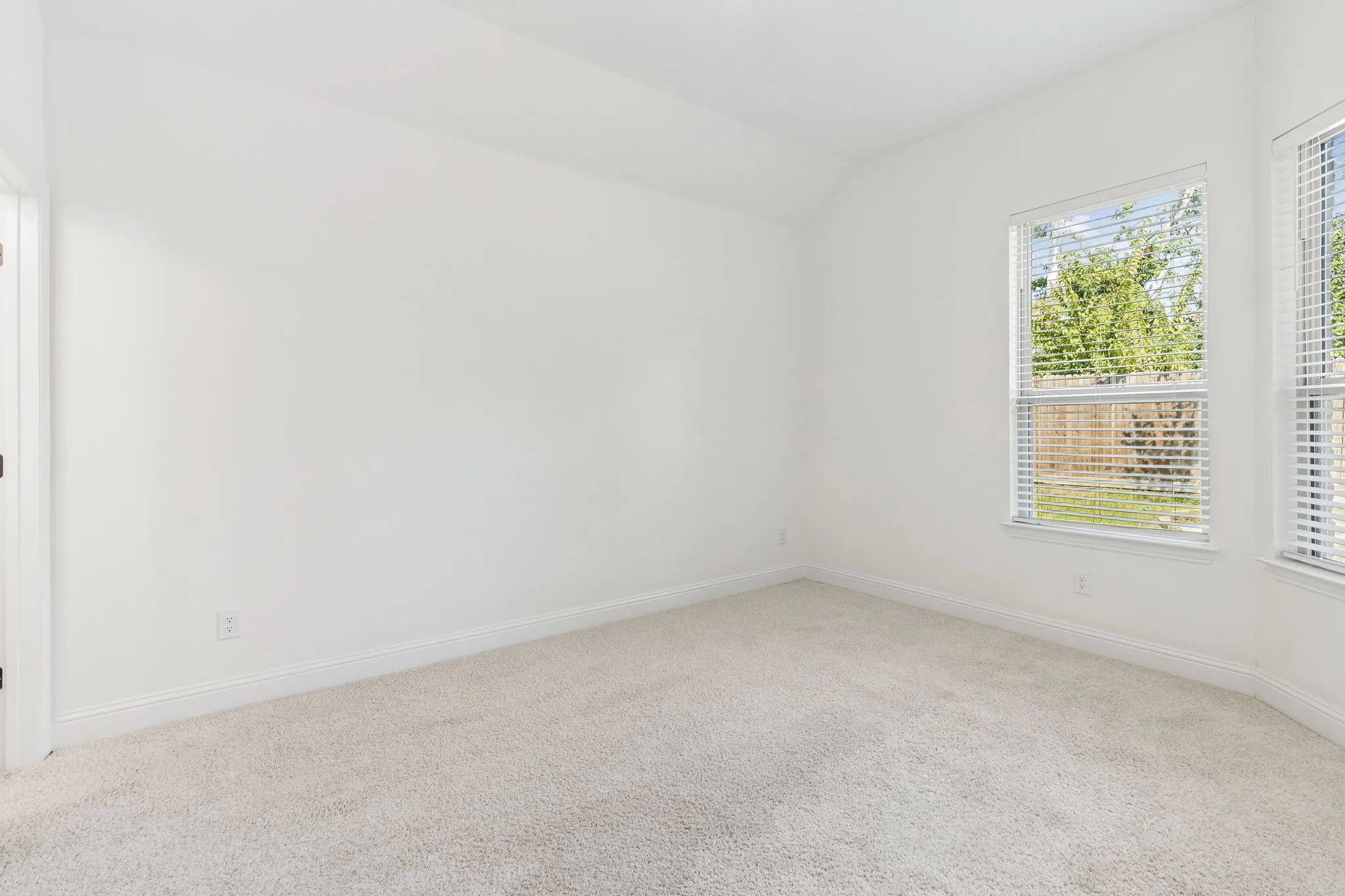 Vaulted ceiling, two windows with blinds, light-toned carpet flooring, white walls, white trim