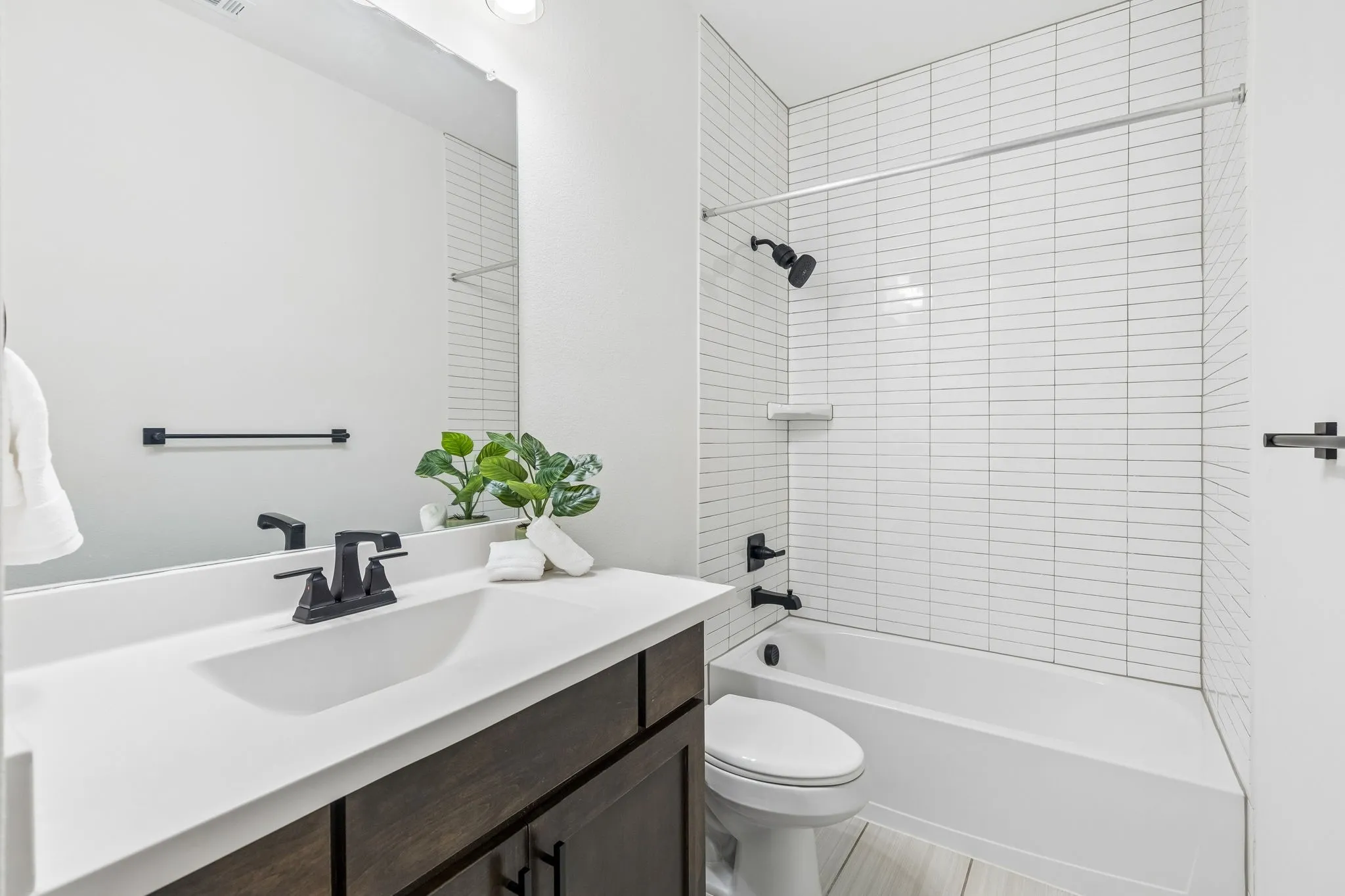 Bathroom featuring a dark wood-finish vanity with a white countertop, matte black fixtures, a built-in tub with a shower, and horizontal white tile surround