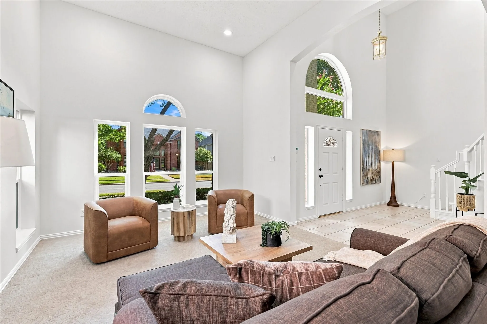 Step into a bright and welcoming entryway where soaring ceilings, fresh modern white walls, and abundant natural light create an airy, open feel. Sunlight pours through the windows, highlighting the spacious formal living room and creating an inviting first impression.