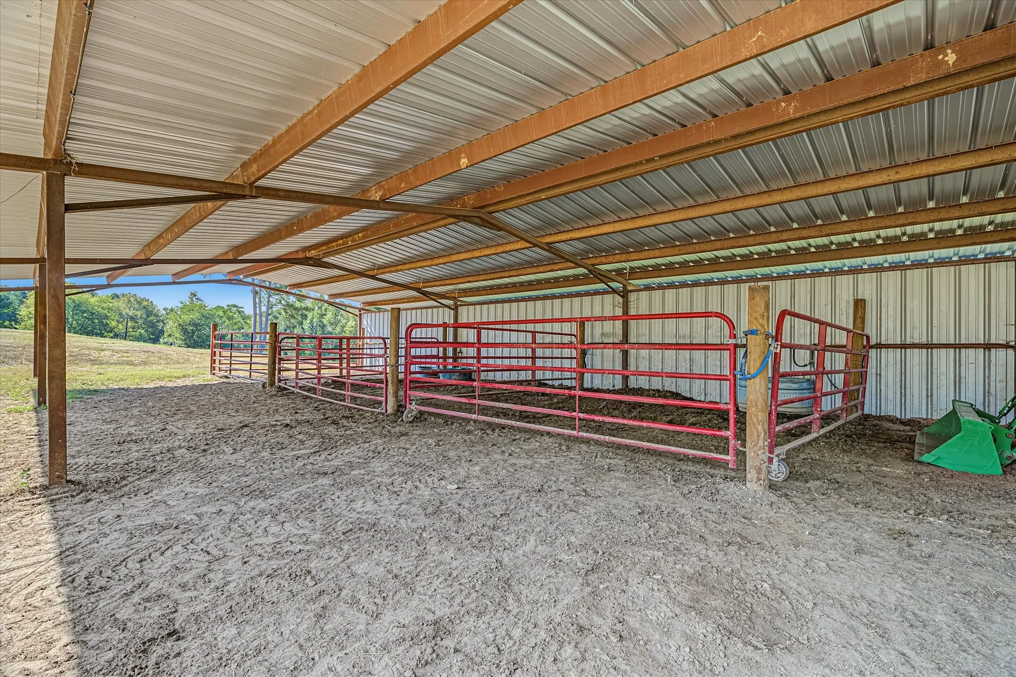 Horse barn with misting system. Sheltered enclosure featuring a metal roof, metal panel walls, and red metal fencing.