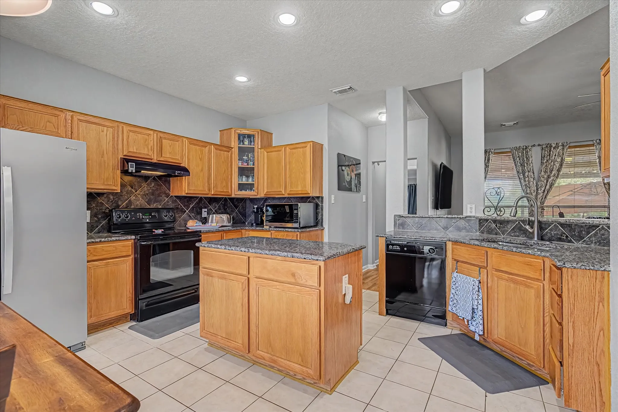 Kitchen featuring an island, light wood cabinetry, granite countertops, tiled flooring, and recessed lighting