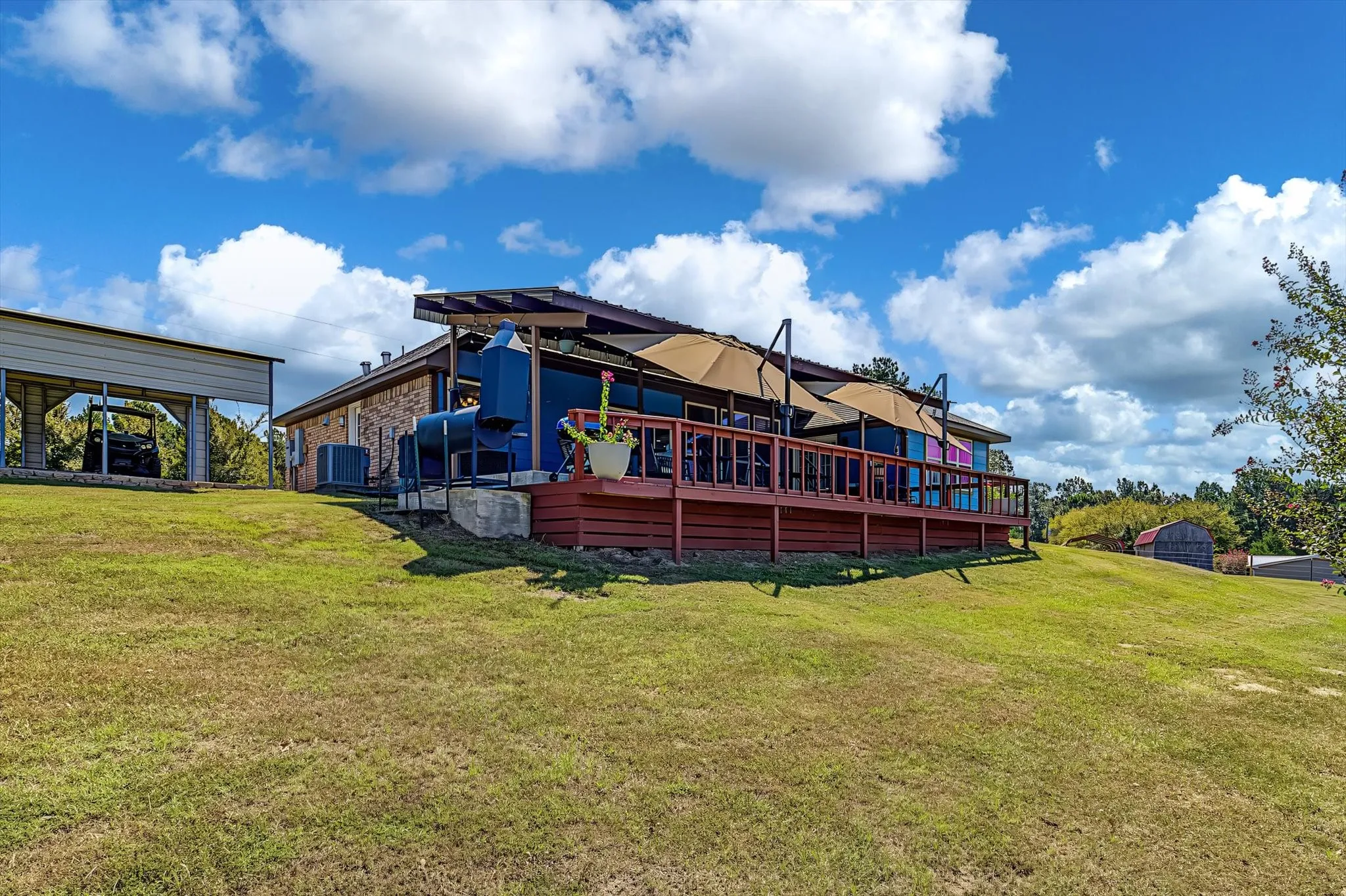 Elevated wood deck with sunshades, brick exterior, and a detached carport structure