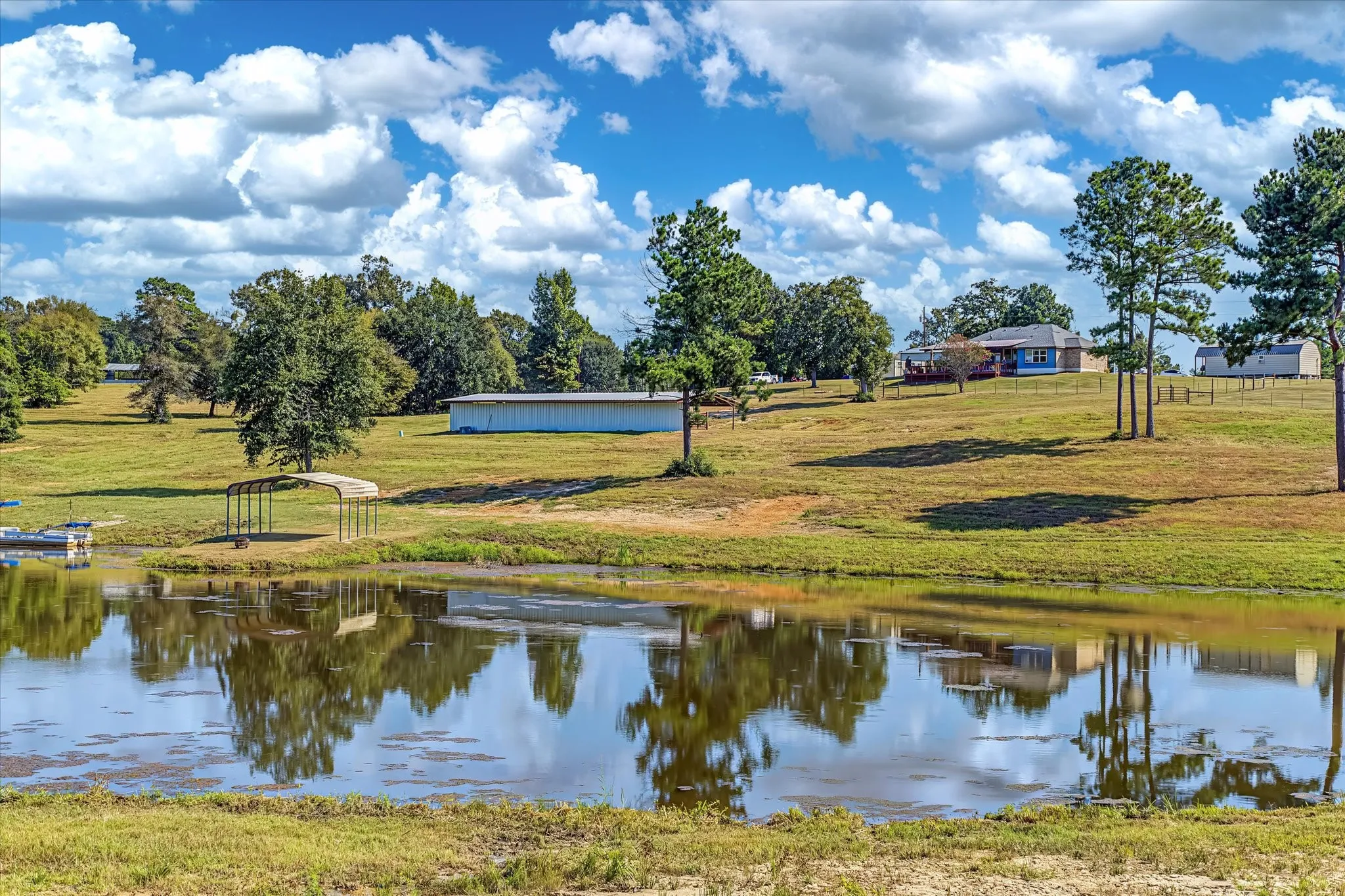 View from back of property looking towards the home featuring a tranquil stocked pond and mature trees.