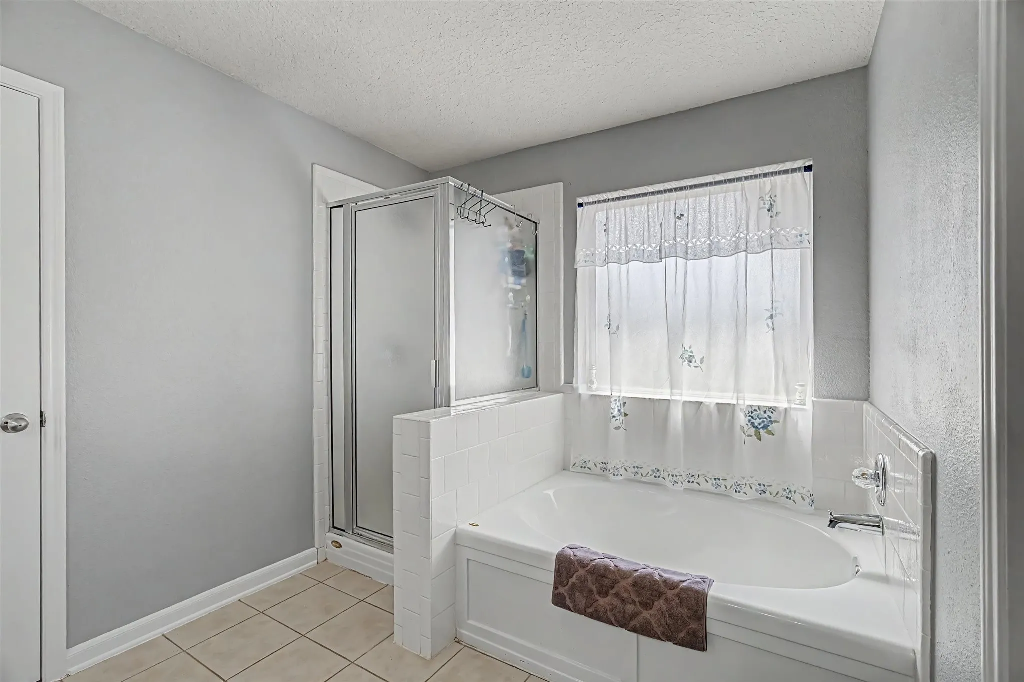 Built-in soaking tub with tile surround, glass-enclosed shower, and tile flooring