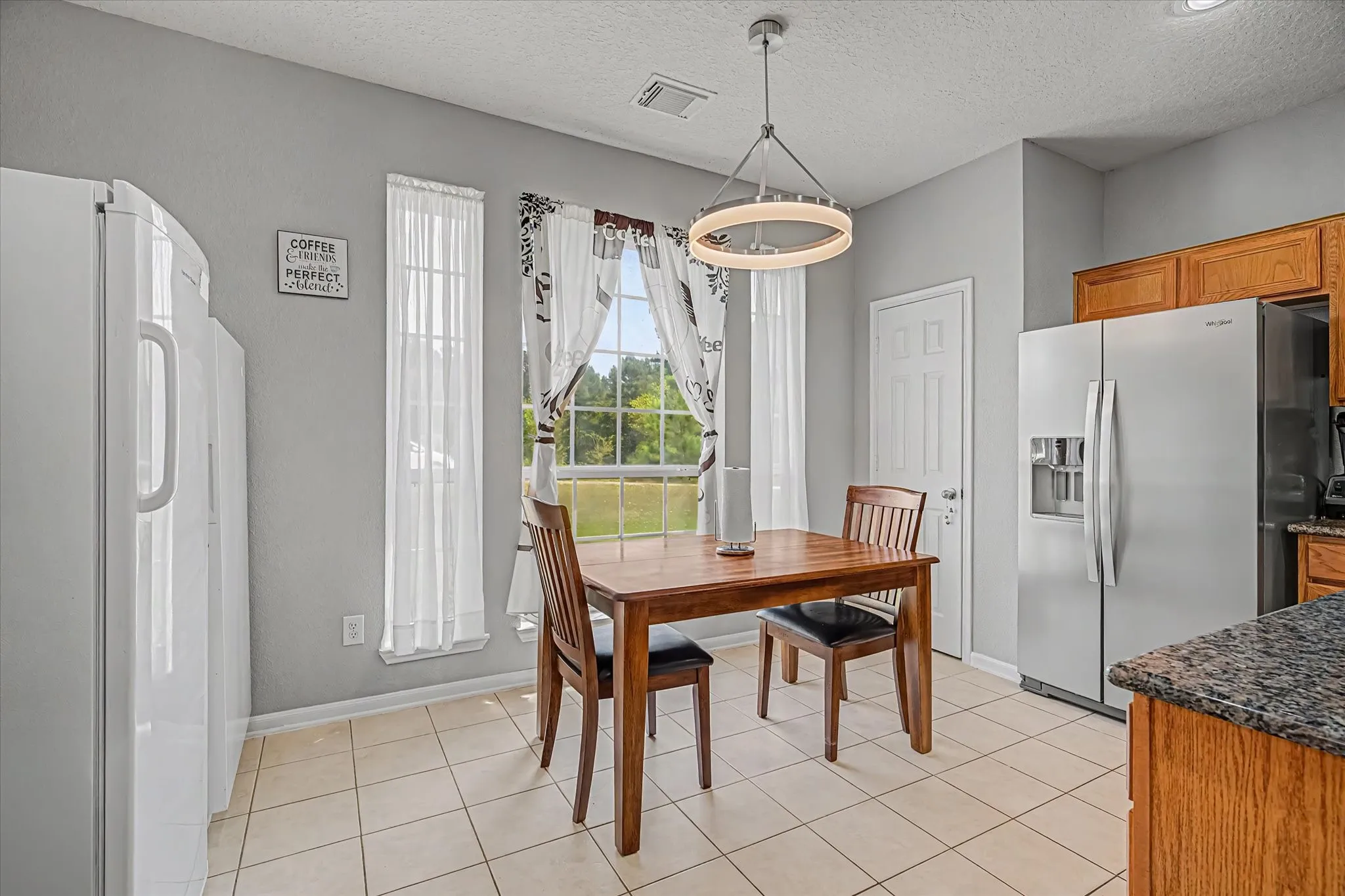 Tile flooring, wood cabinetry, stainless steel refrigerator, and recessed lighting