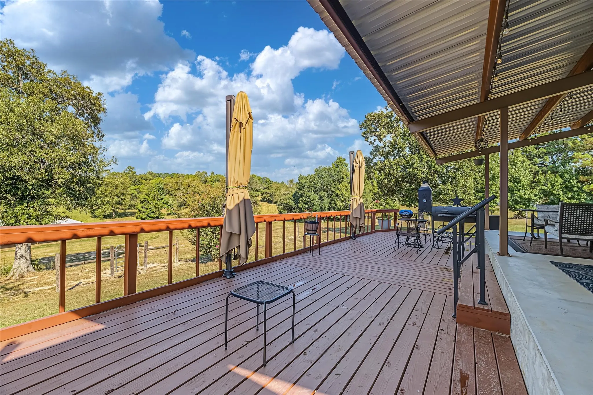 Expansive wood deck with a metal roof overhang, featuring a wood railing with metal balusters. Extended Decking to back patio with large umbrella for added shading.