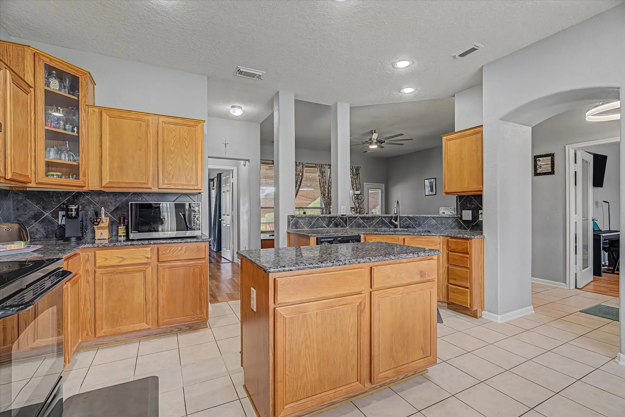 Kitchen featuring light wood cabinetry, granite countertops, tile backsplash, a central island, and recessed lighting