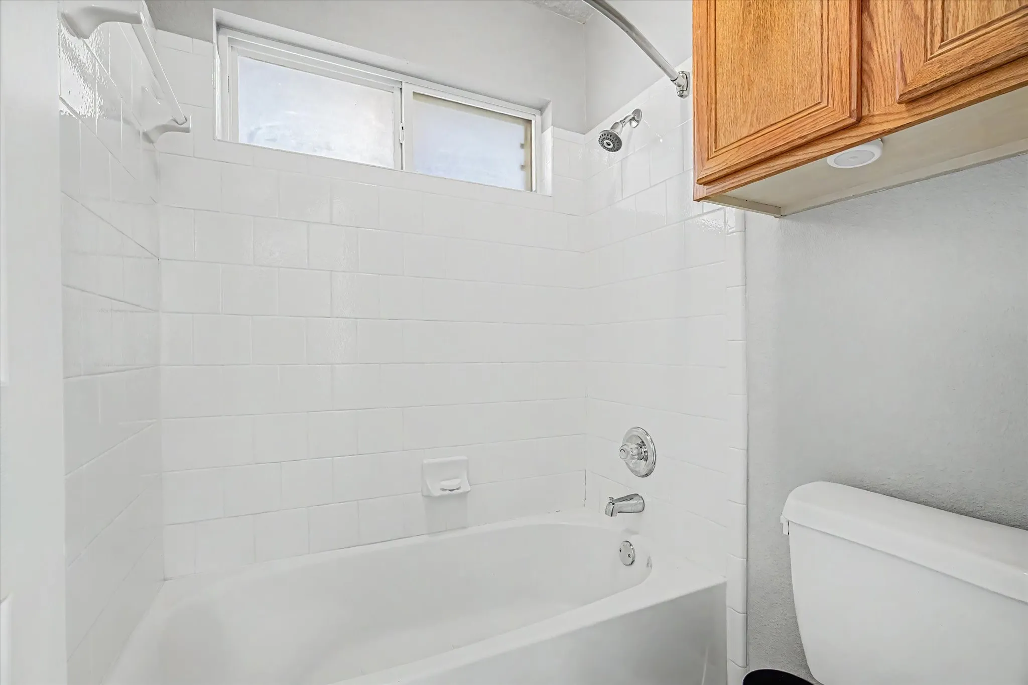 Shower and tub combo with white tile surround, chrome fixtures, and an upper transom window