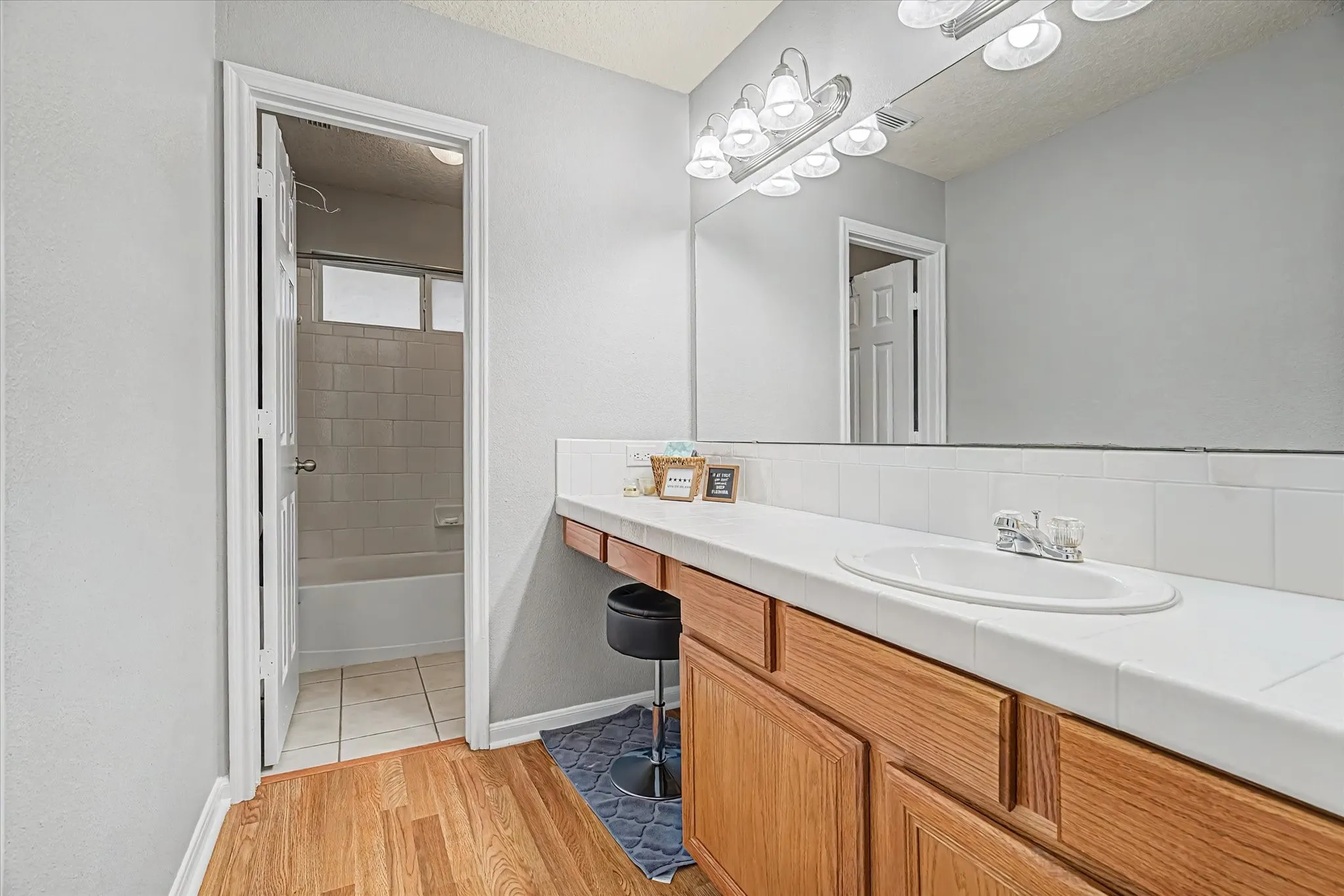 Secondary hall bath w/ vanity featuring a ceramic sink, tile countertop, and full-width mirror