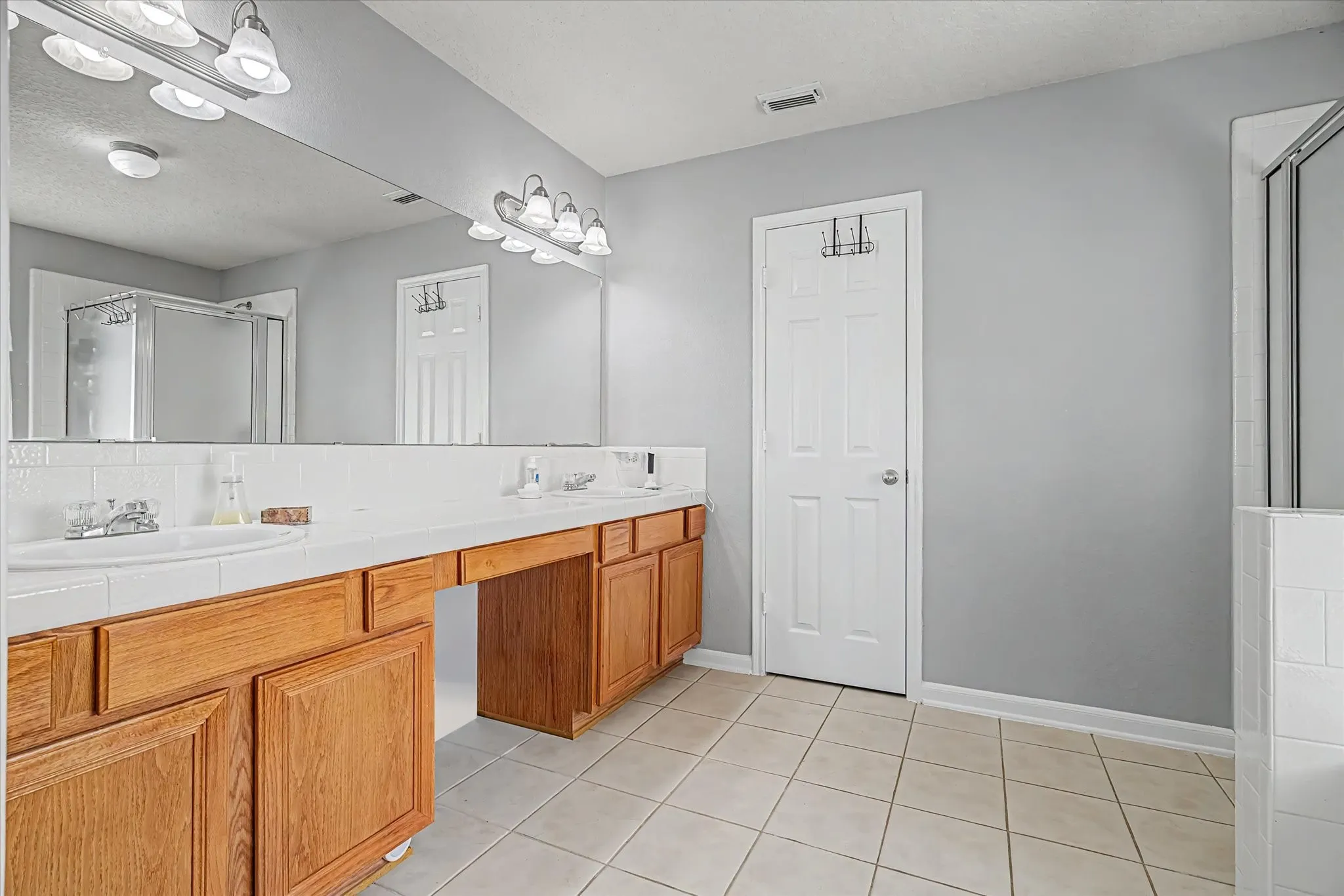 Primary Bath w/ double vanity with wood-finish cabinetry and tile flooring