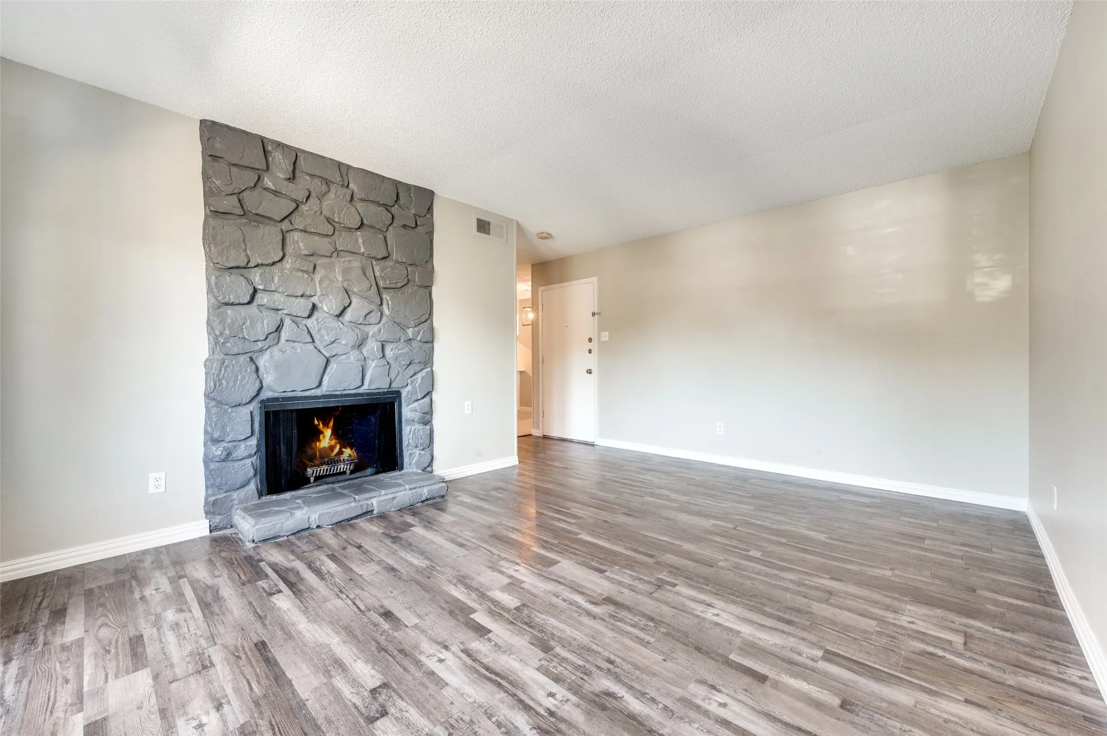 Stone-clad fireplace with hearth, wood-finish flooring, and painted walls