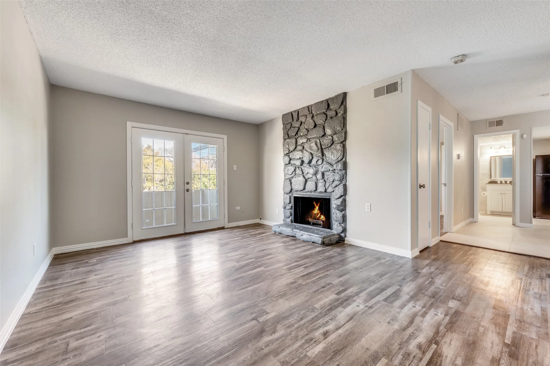 Wood-finish flooring, stone-clad fireplace, light-colored walls, white French doors, and recessed lighting