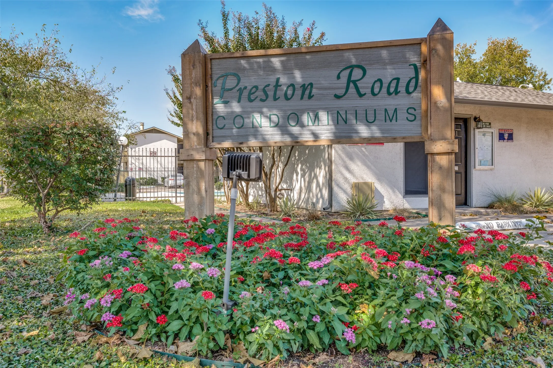 Wood-frame community sign with raised lettering, surrounded by a landscaped bed of colorful flowering plants