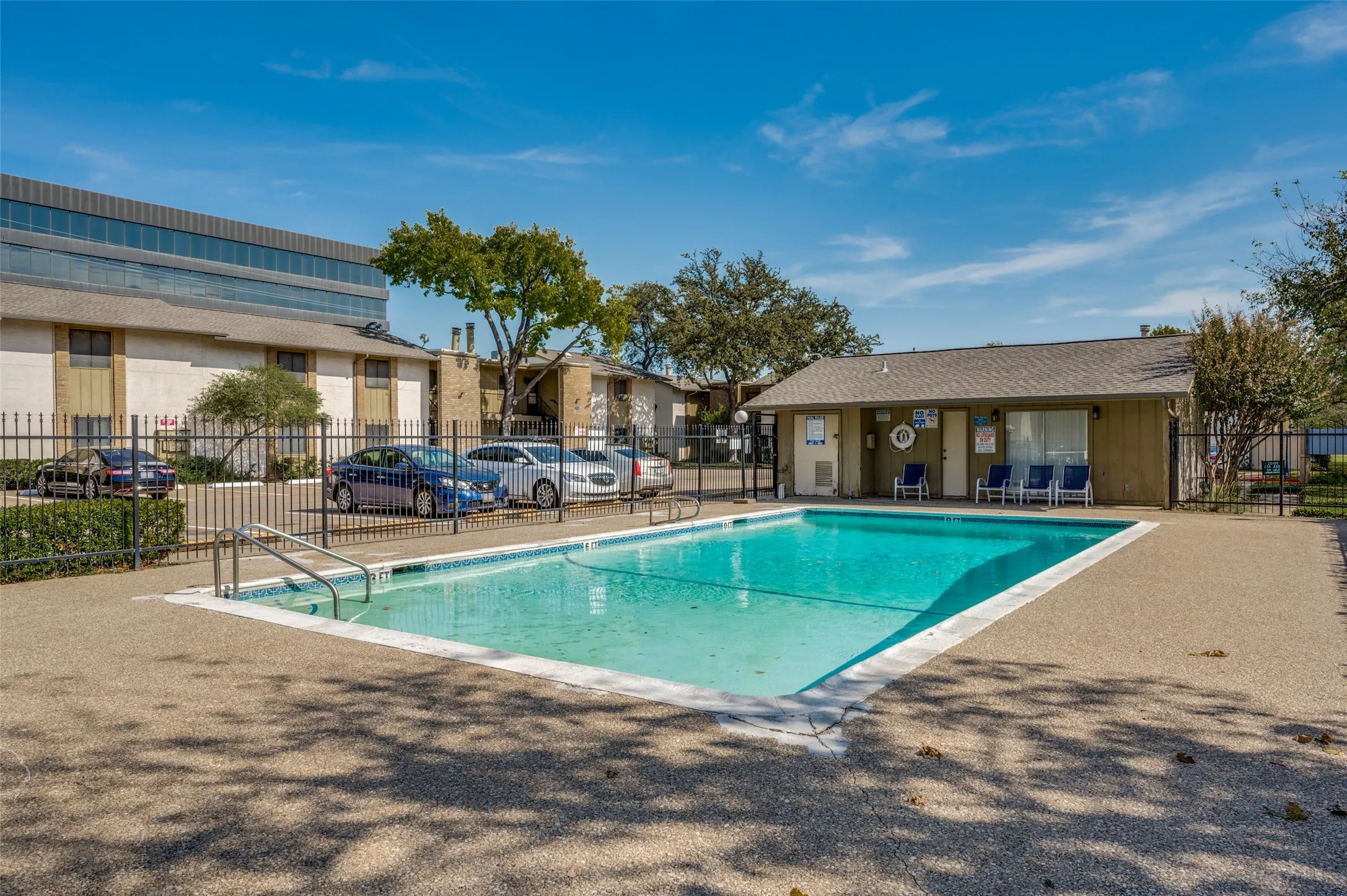 Outdoor swimming pool with concrete decking, perimeter fencing, and an adjacent structure