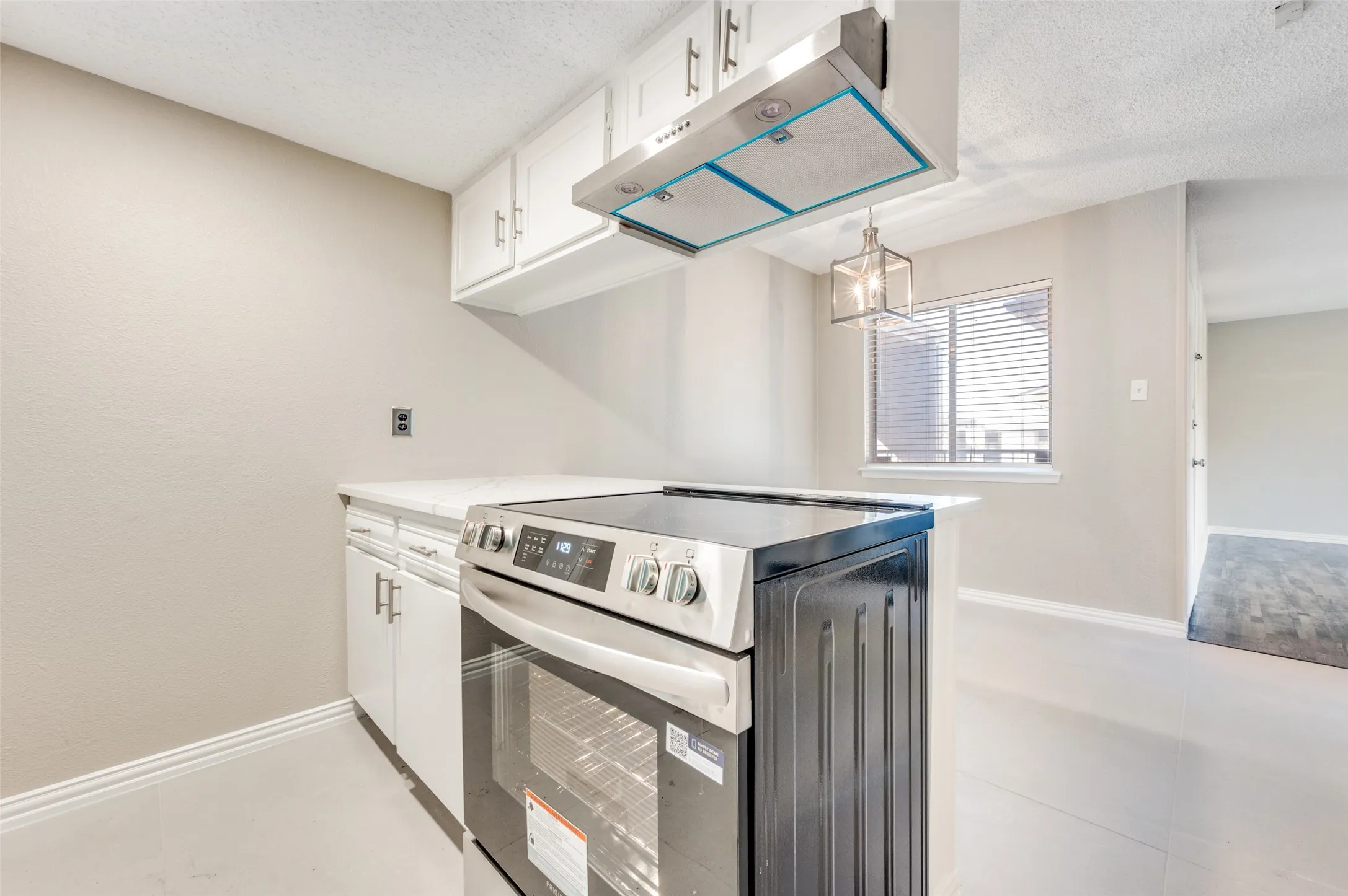 Stainless steel range with a coordinating range hood, white cabinetry, light-toned countertop, and pendant lighting