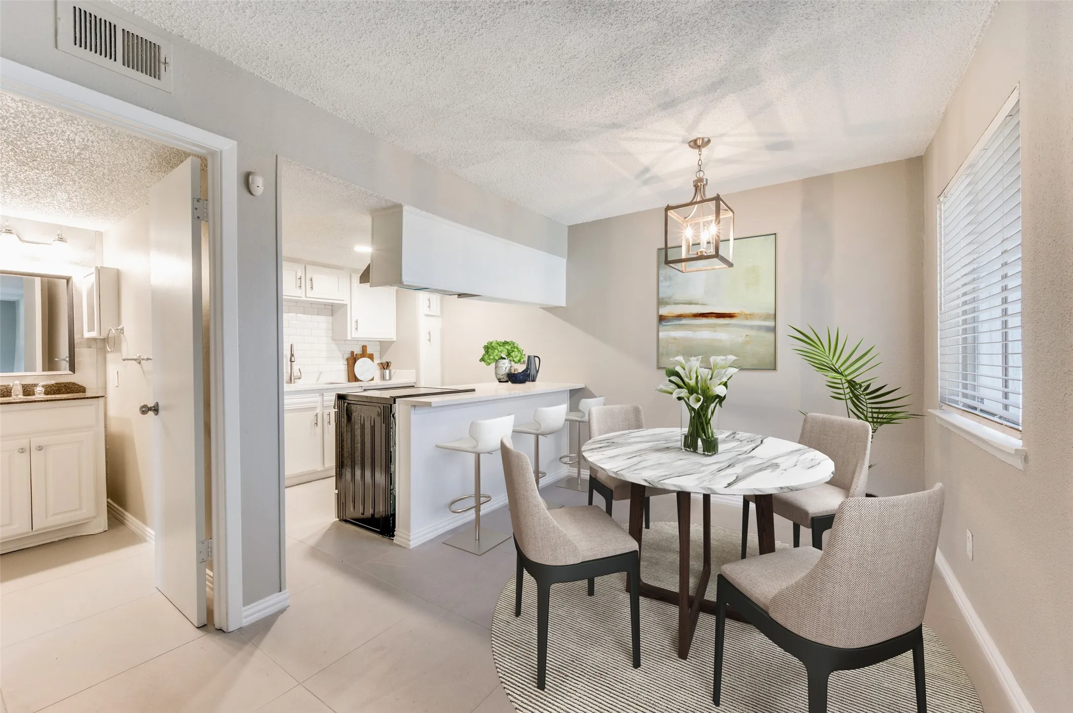 Dining area with a modern chandelier, adjacent to a kitchen featuring white cabinetry, a breakfast bar, and tile flooring