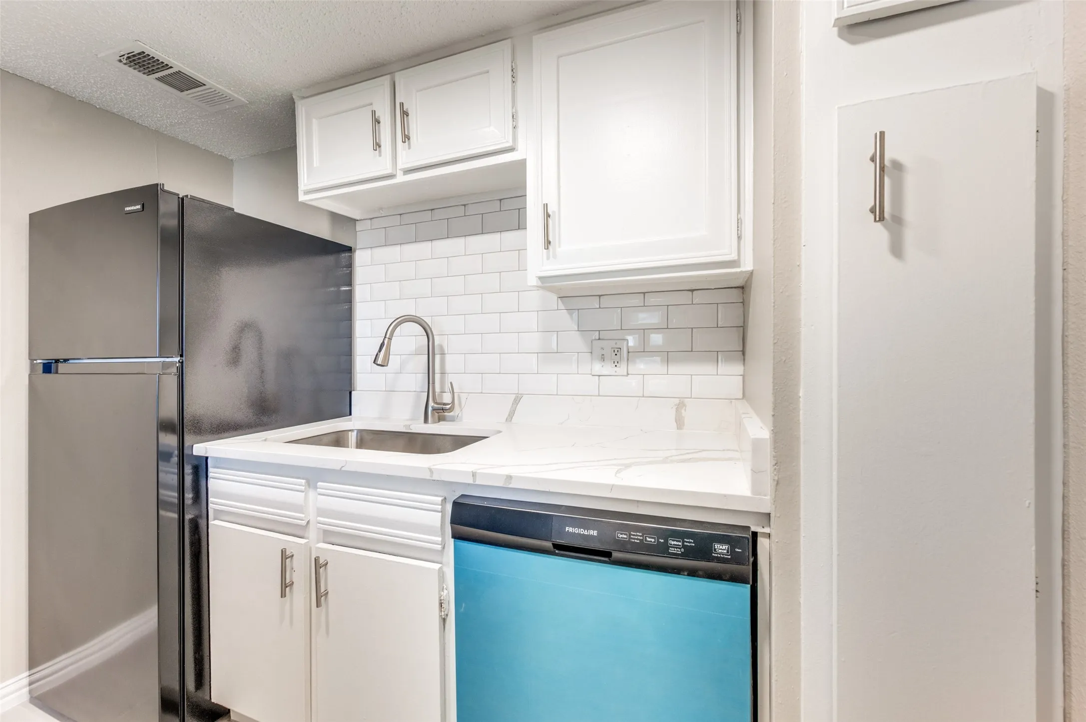 White cabinetry, stainless steel sink, white subway tile backsplash, light-toned countertop, and stainless steel refrigerator