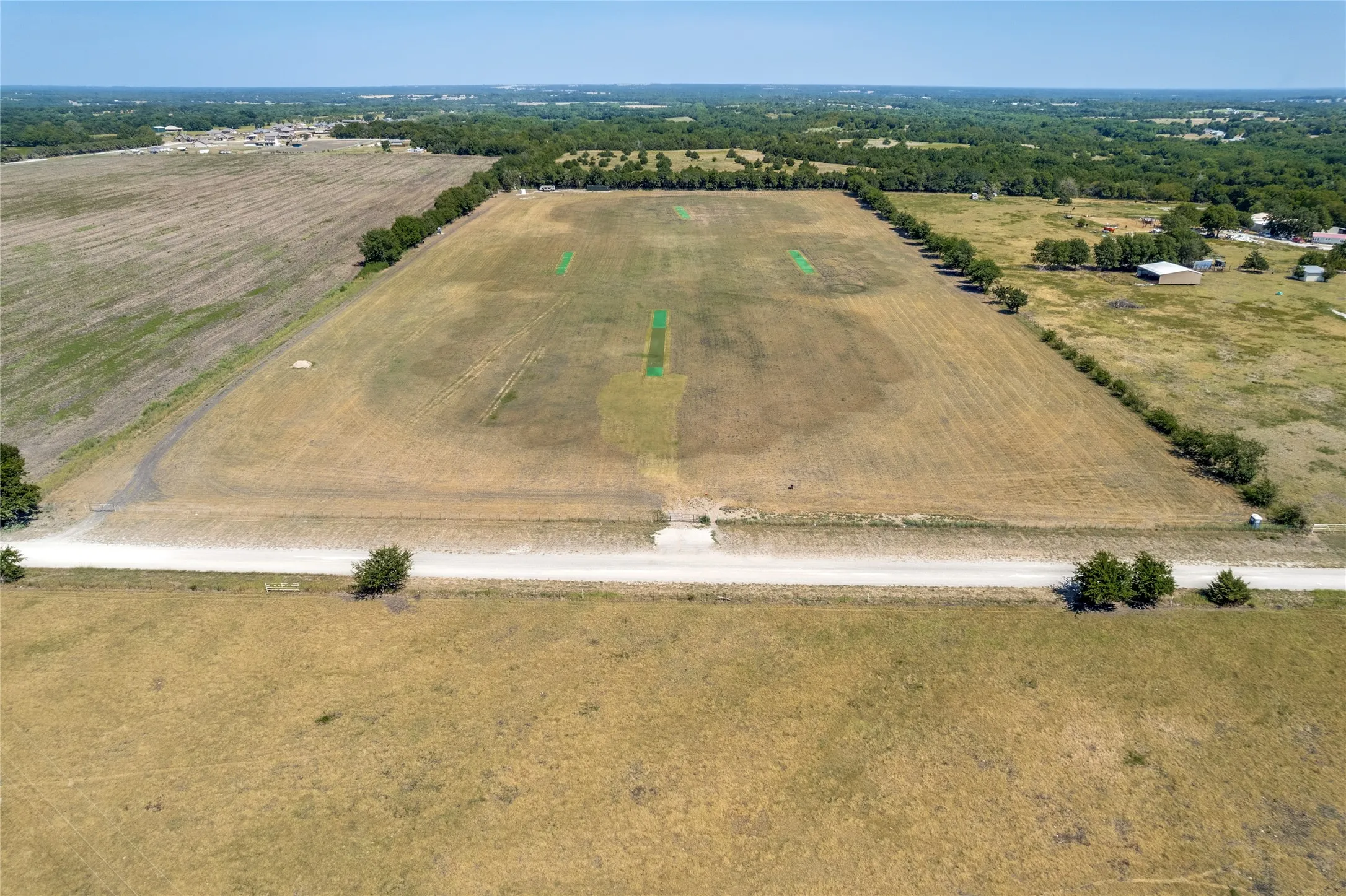 Expansive open field with partial green grass sections, defined by a treeline on two sides