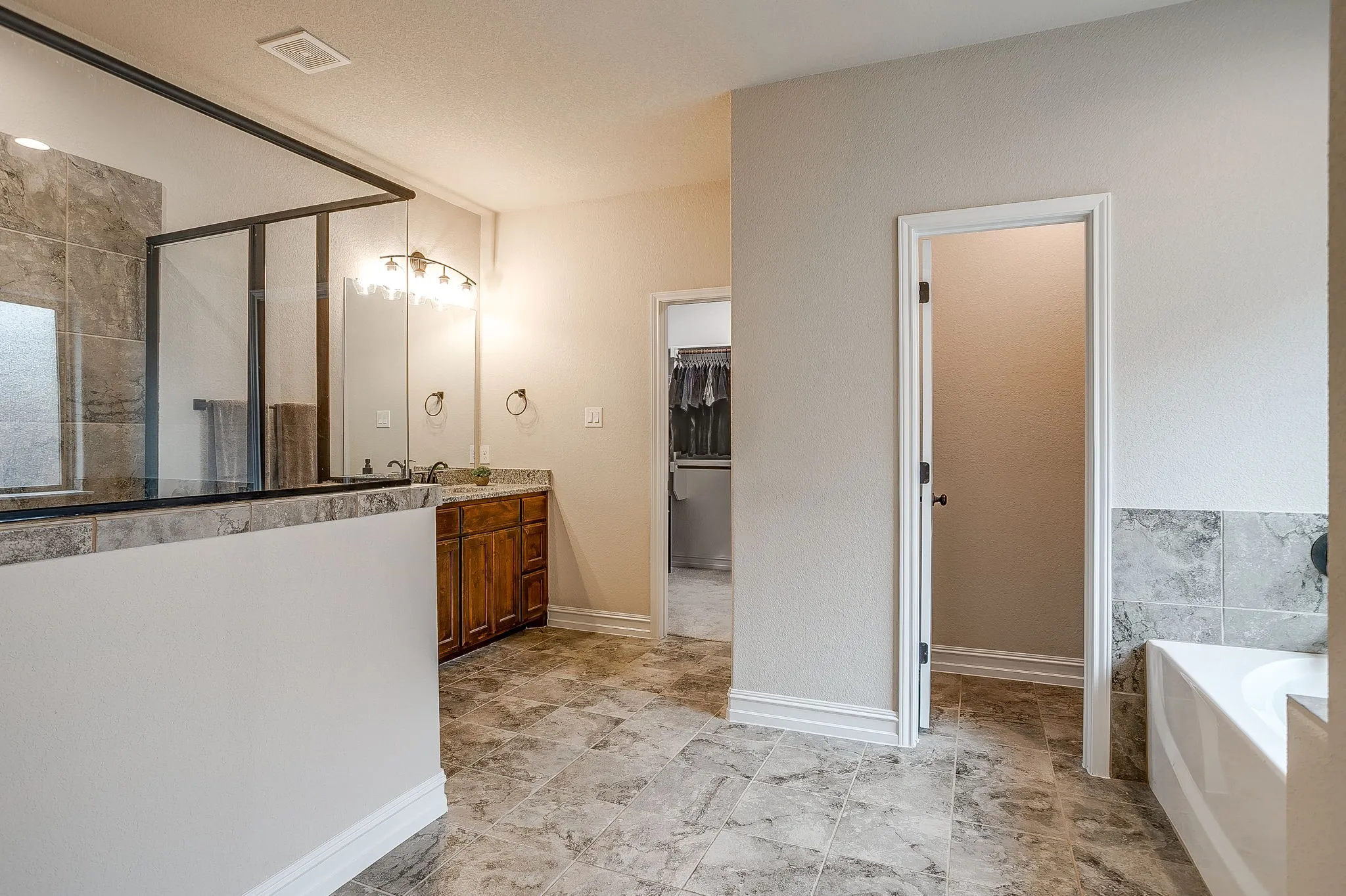 Spacious bathroom featuring tiled flooring, a walk-in shower with a glass enclosure, a double vanity with an integrated sink, and a built-in bathtub