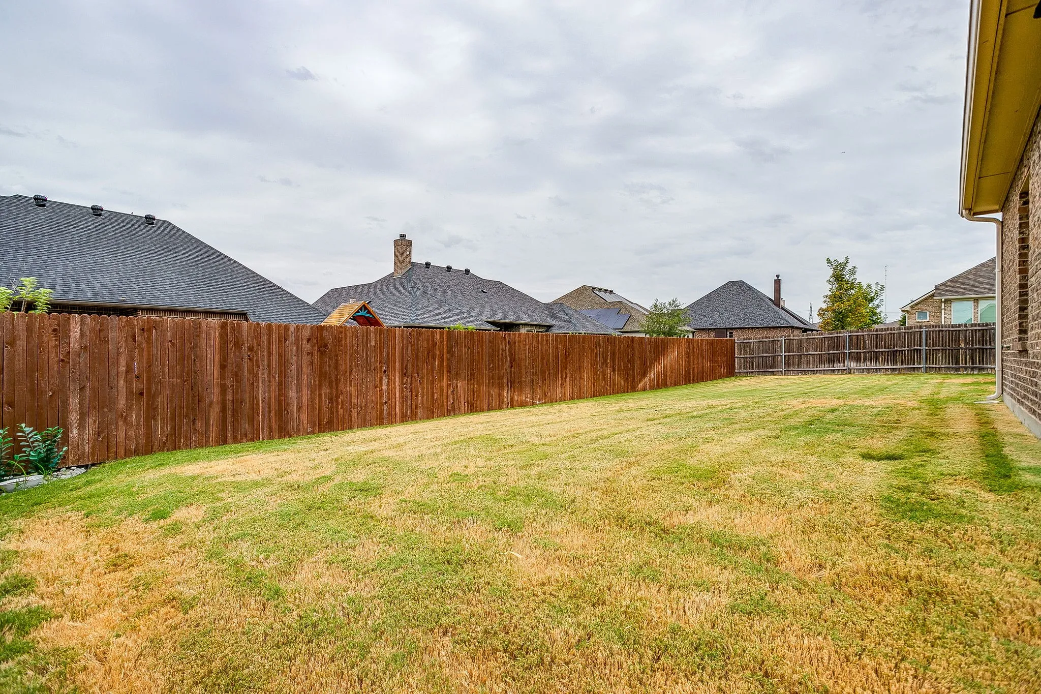 Expansive backyard featuring a manicured lawn, wood fencing, and a brick exterior