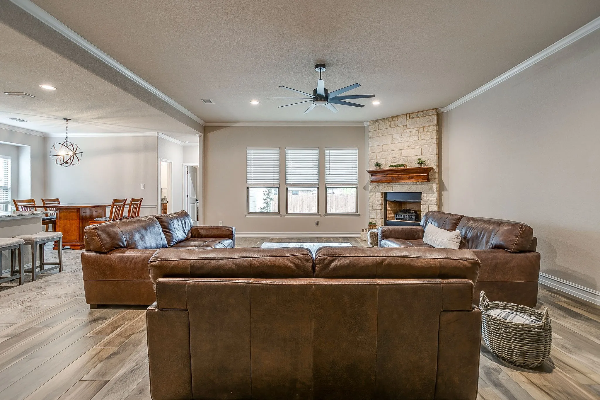Spacious living area featuring wood-finish flooring, a stone fireplace with a wood mantel, and multiple windows