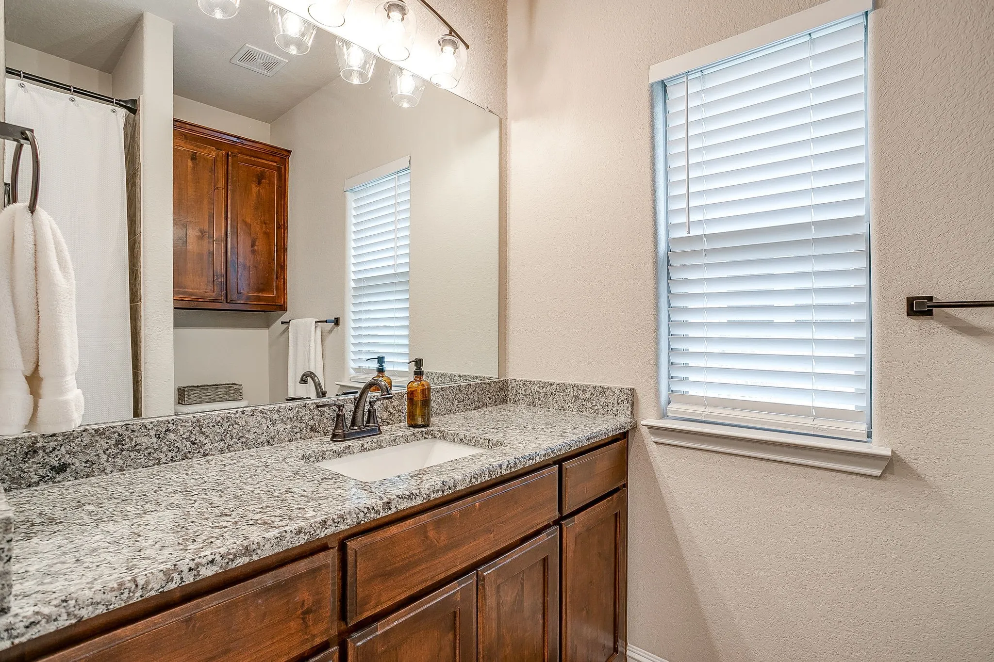 Single vanity with a light granite countertop, undermount sink, and dark wood-finish cabinetry