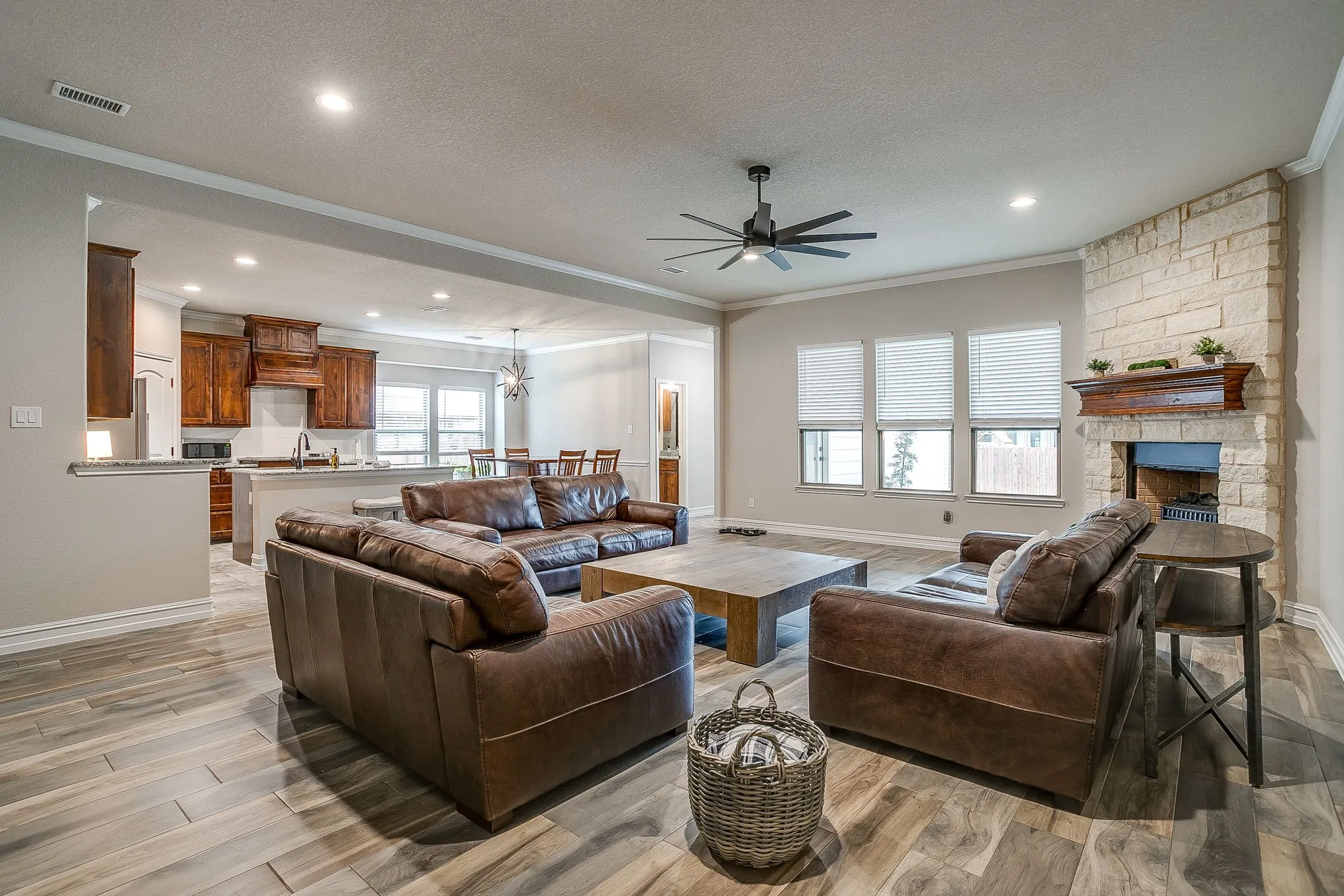 Open-concept living space featuring wood-finish flooring, a stone-clad fireplace with a wood mantle, and recessed lighting
