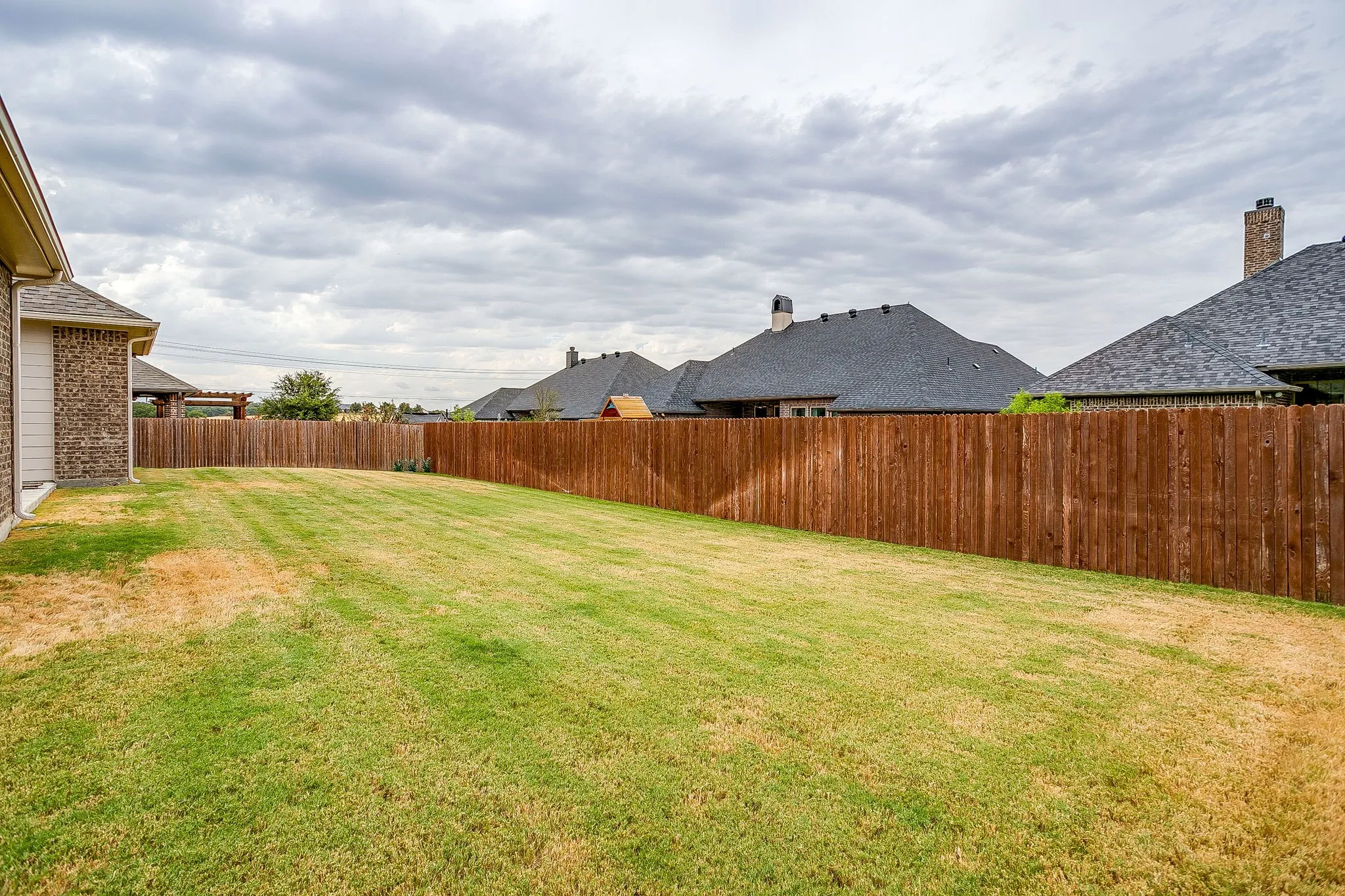 Expansive backyard featuring a lush lawn, privacy fencing, and a brick-clad exterior