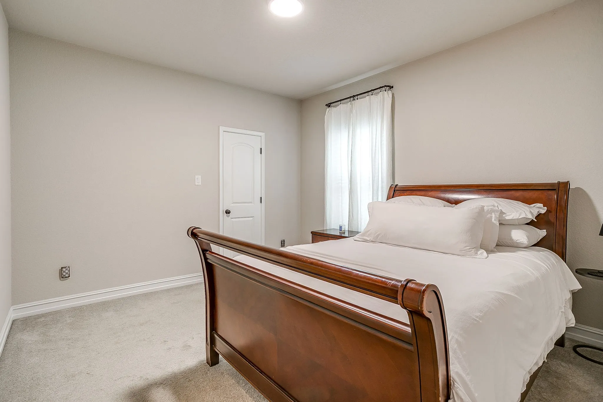 Recessed ceiling lighting, light-toned wall paint, white trim, carpeted flooring, and a window with sheer curtains