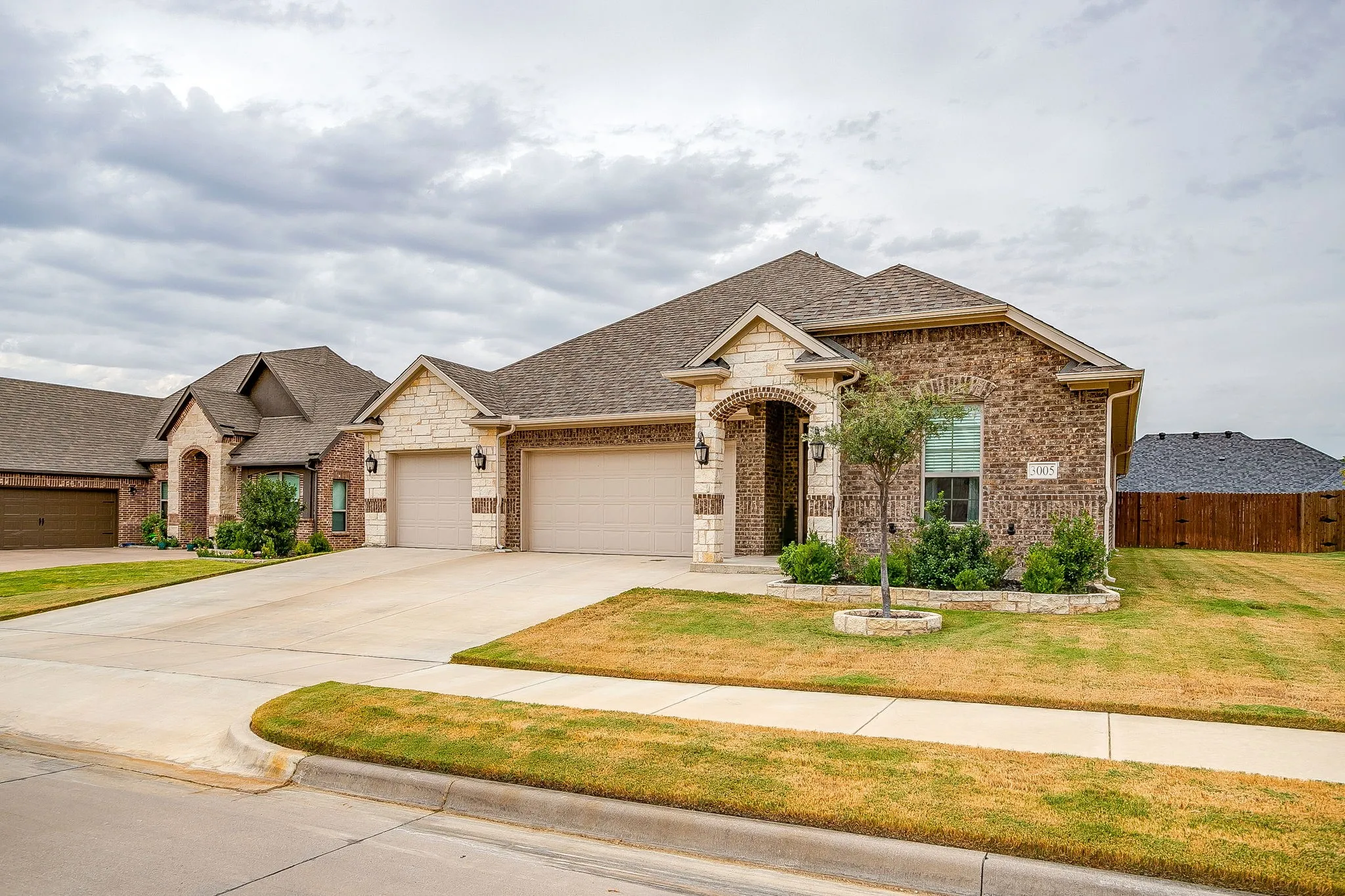 Brick and stone facade with arched entry, dual garage doors, concrete driveway, and established front landscaping