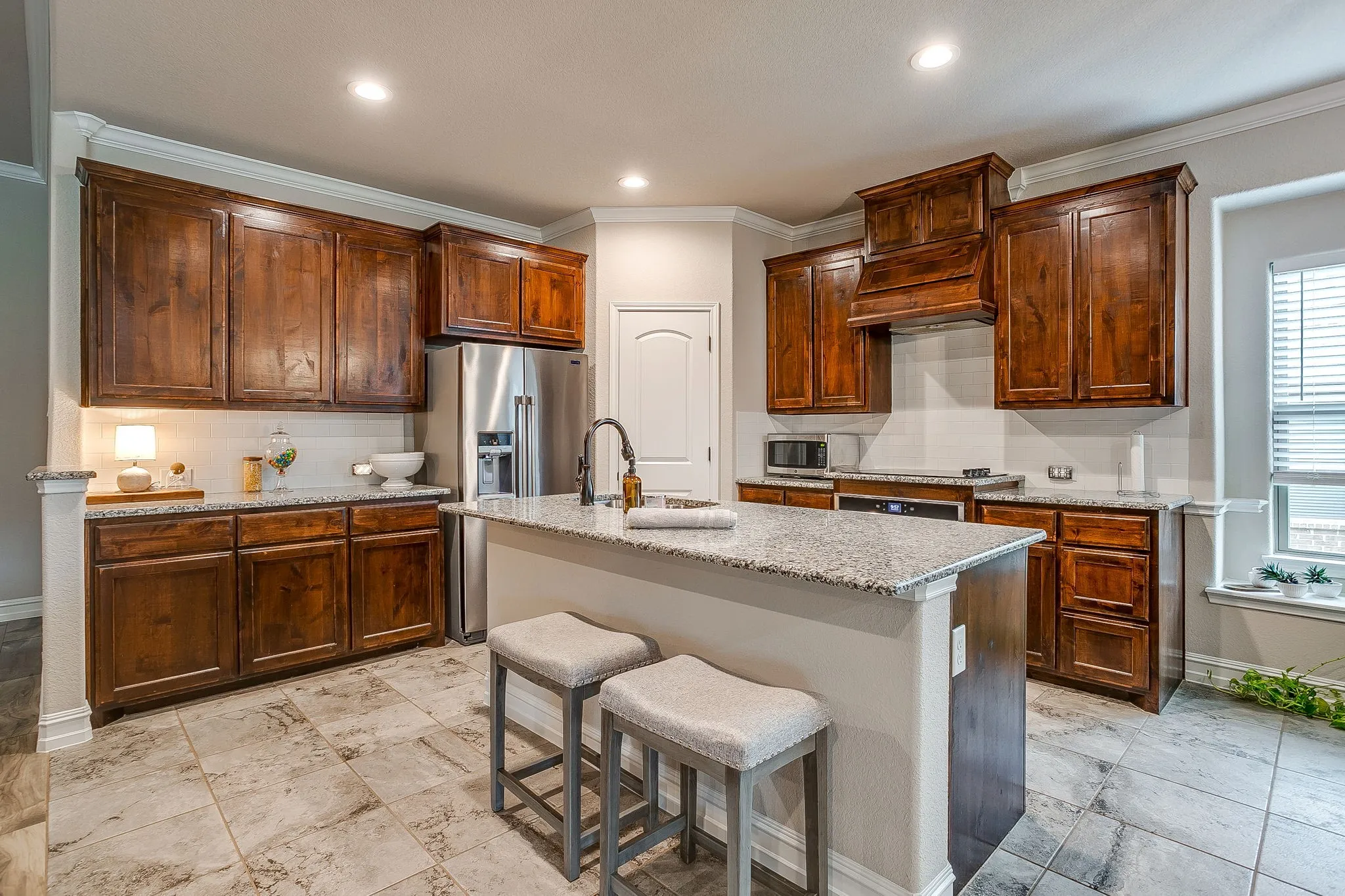 Kitchen featuring wood cabinetry, granite countertops, stainless steel appliances, a center island with a sink, and tile flooring
