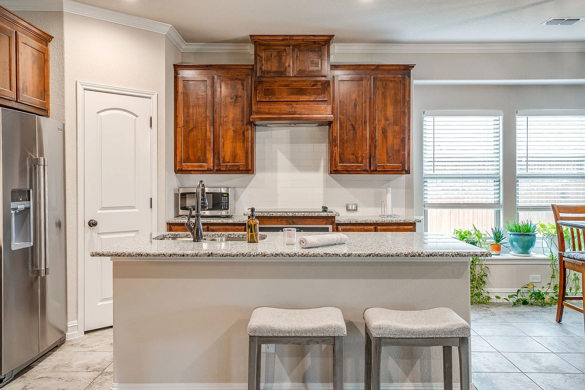 Kitchen featuring wood cabinetry, stainless steel appliances, a center island with a sink, white countertops, and tile flooring