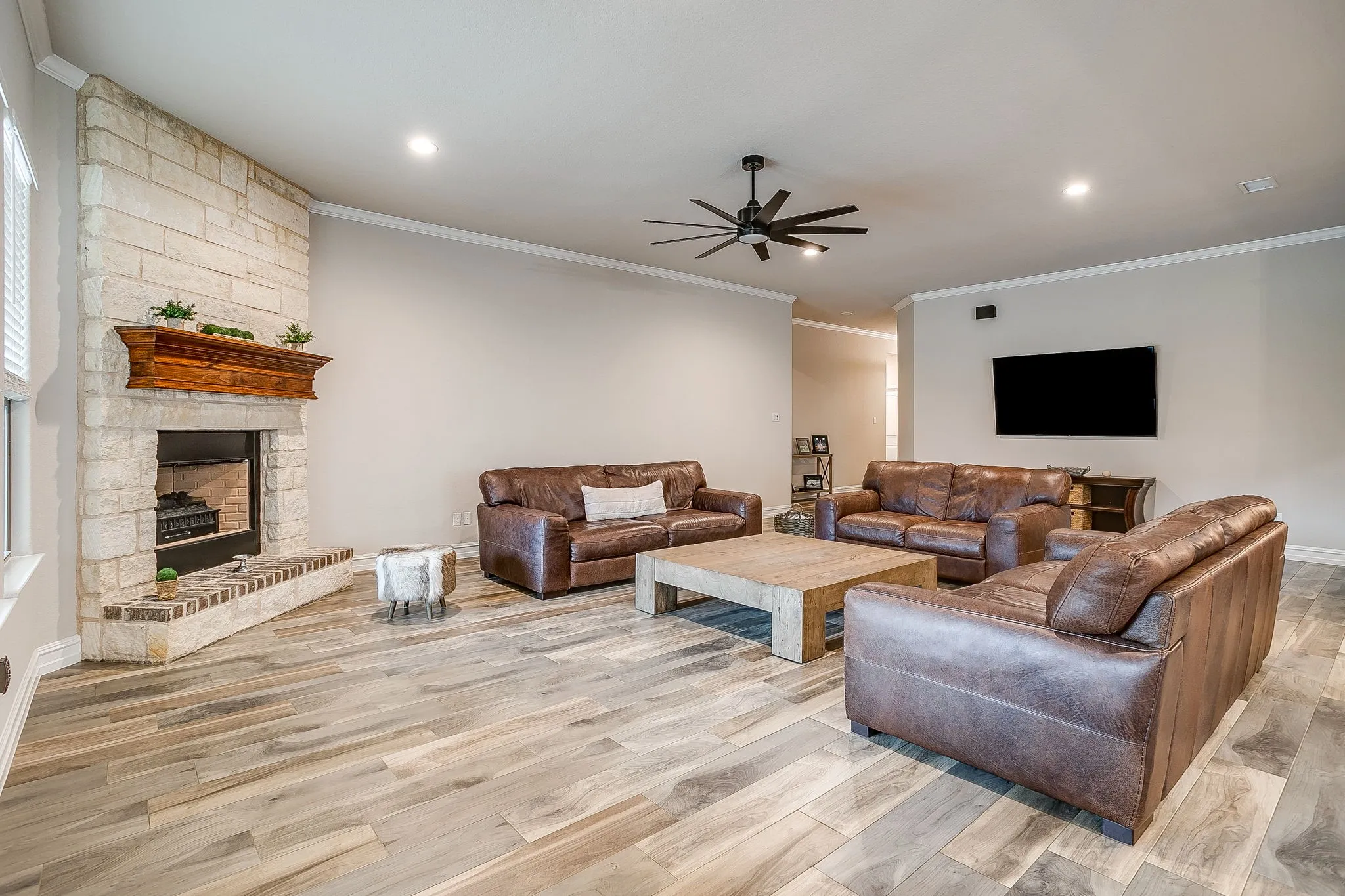 Stone-clad fireplace with a wood mantle, wood-finish flooring, recessed lighting, and a ceiling fan
