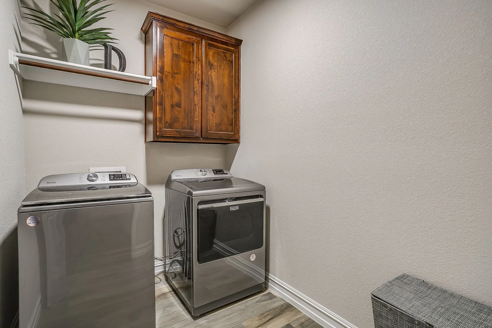 Laundry area with wood-finish flooring, a wall-mounted wooden cabinet, and a white wall shelf