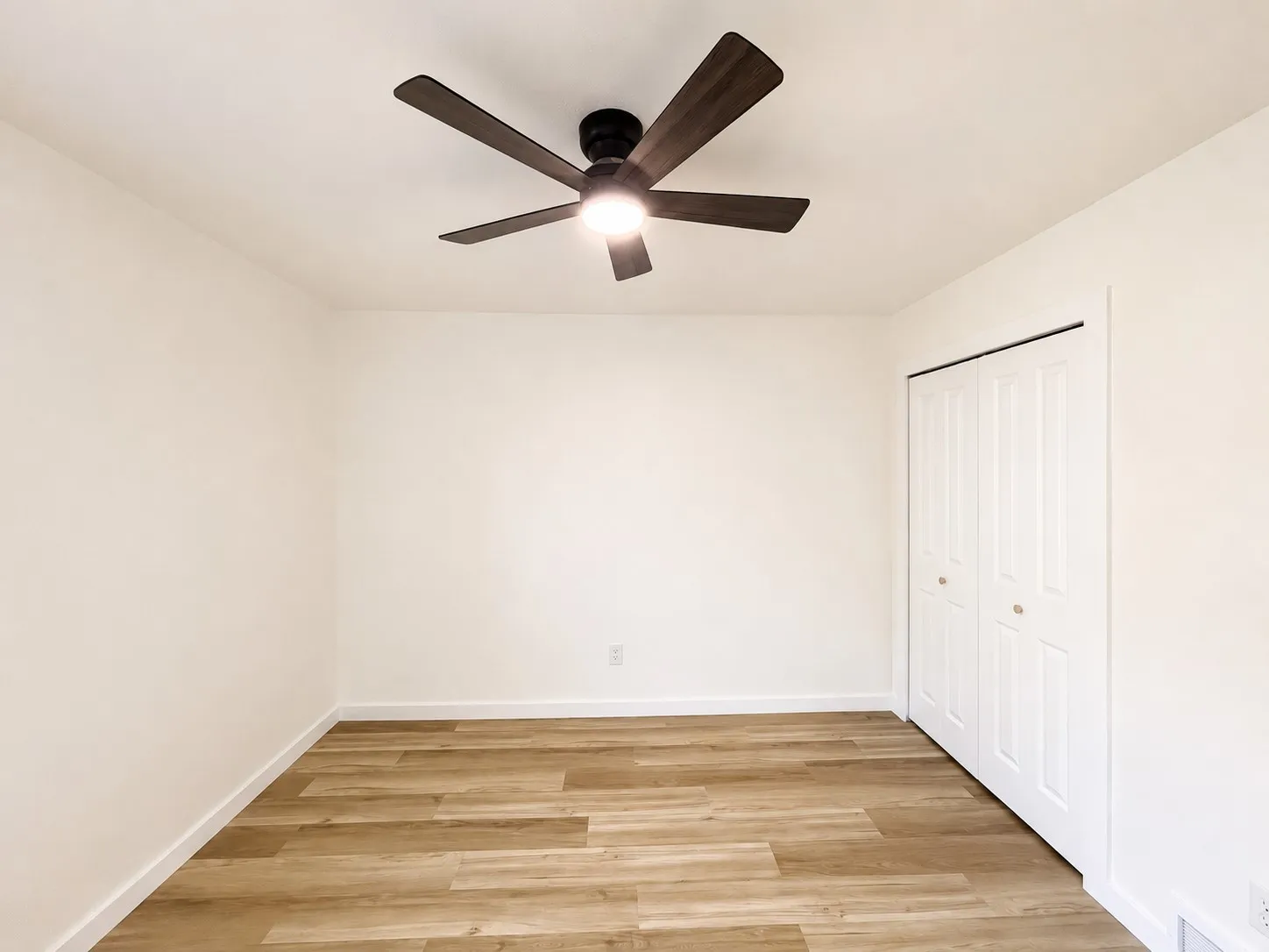 Wood-finish flooring, ceiling fan with integrated lighting, and a bi-fold closet door