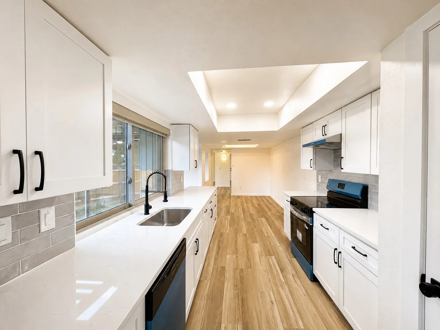 Galley kitchen featuring white shaker cabinetry, white countertops, a stainless steel sink with a gooseneck faucet, and wood-finish flooring